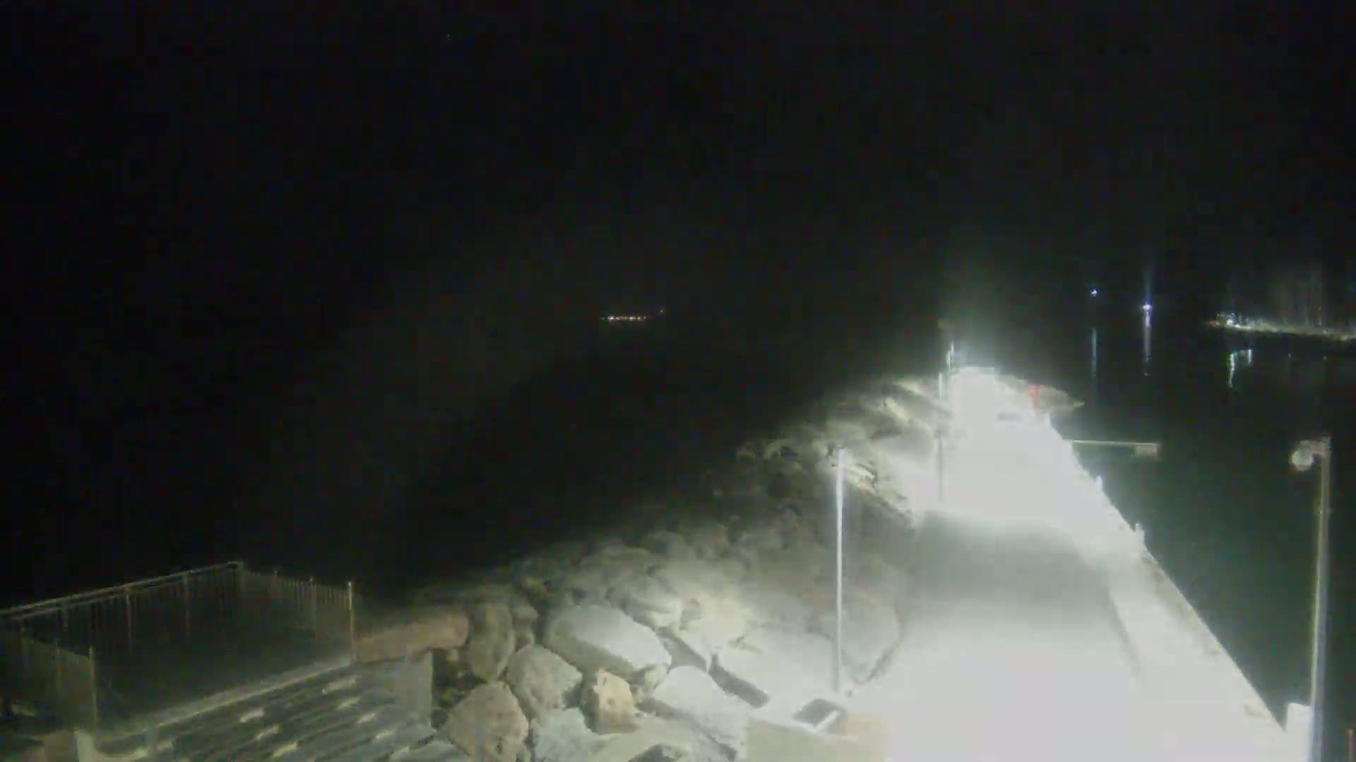 A brightly lit pier extends over dark water at night, with a rocky shoreline visible on one side.