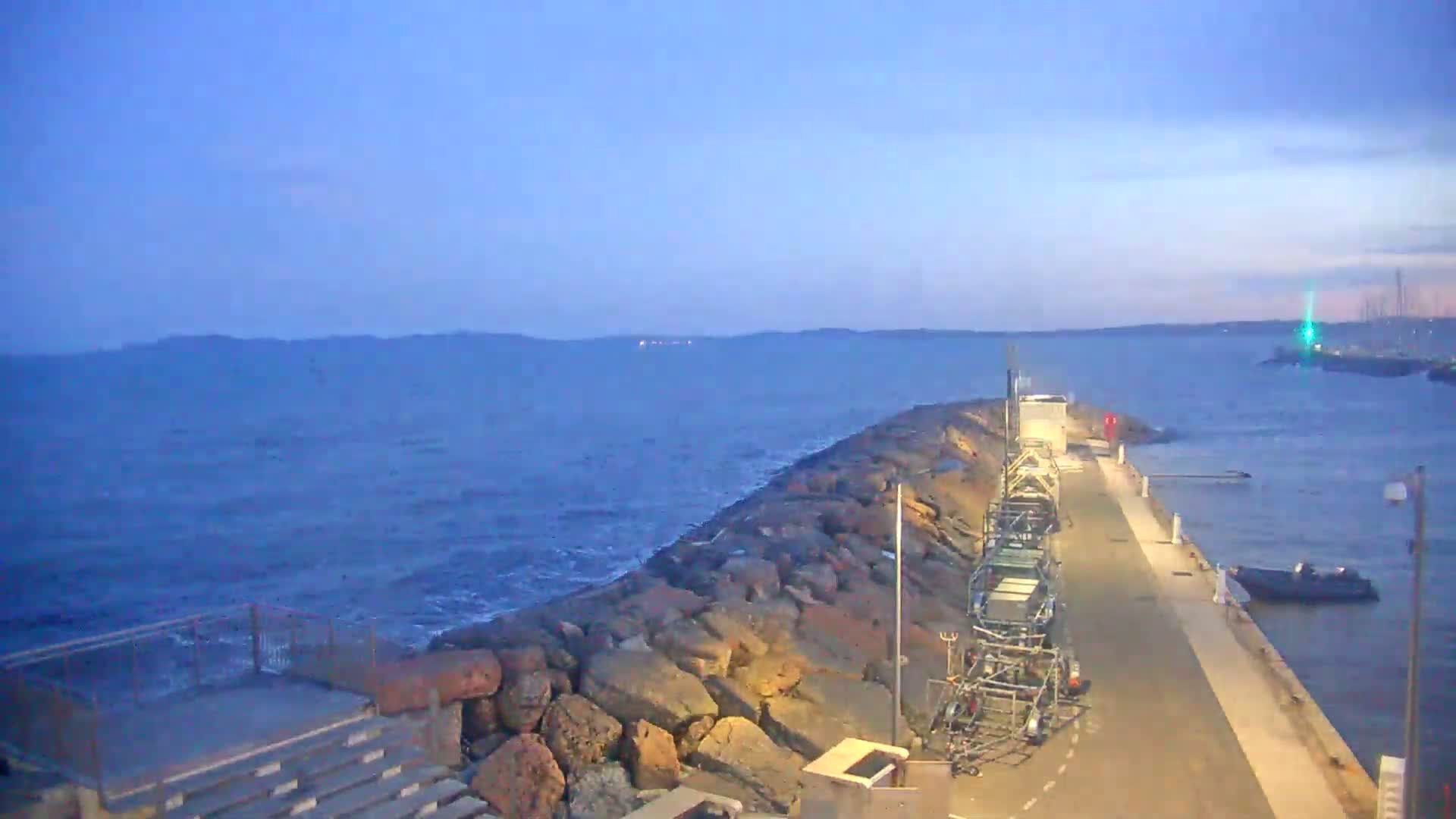 A rocky breakwater extends into a calm, dark blue sea under a twilight sky.