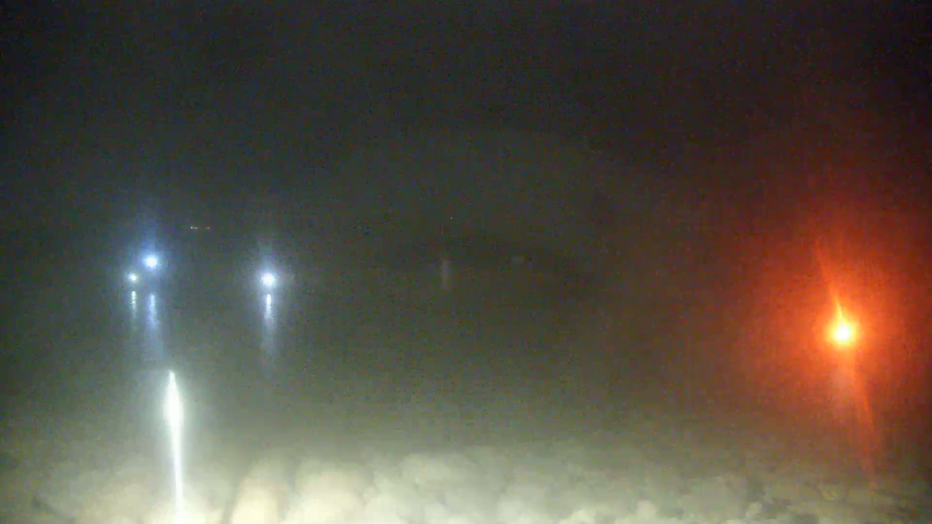 Two bright lights and a dim orange light are visible through a hazy, dark night.