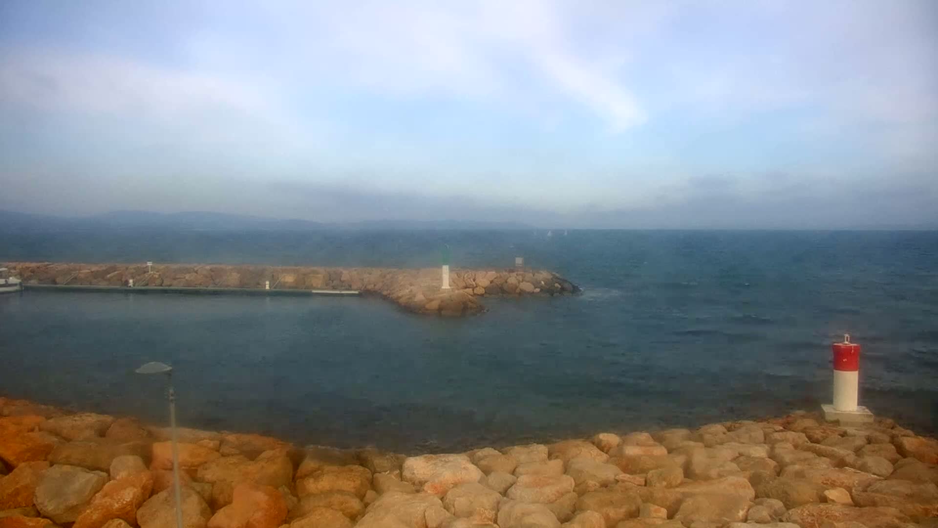 A rocky breakwater juts into a somewhat choppy sea under a hazy sky.