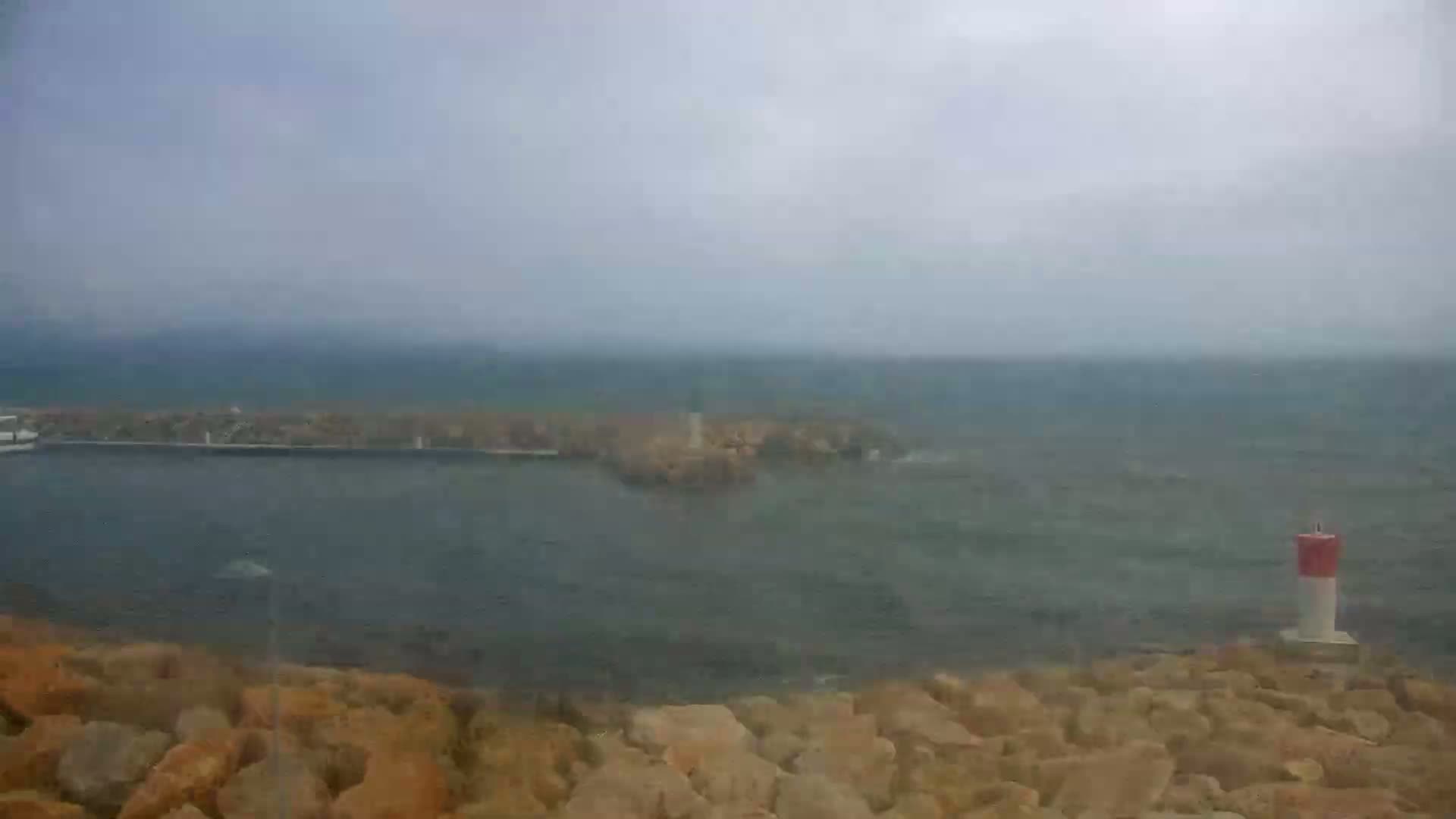 A hazy, overcast day reveals a small harbor with a breakwater, a lighthouse, and a buoy, all partially obscured by mist.