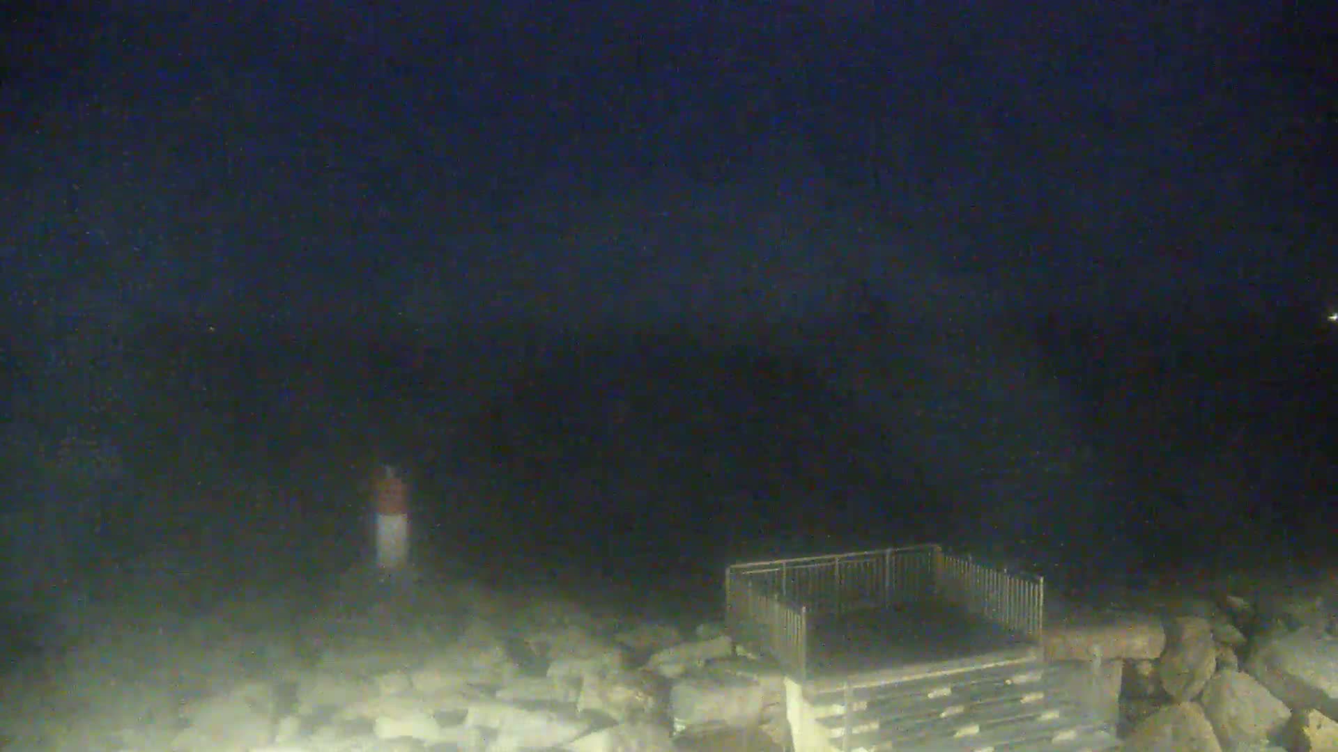 A person stands near a dark, rocky shoreline at night under a dark sky.