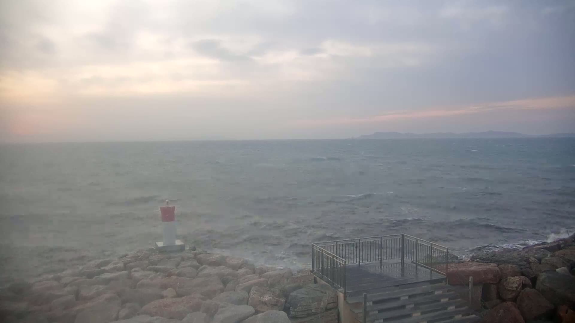 A rocky shoreline with a small viewing platform overlooks a choppy sea under a cloudy, overcast sky.