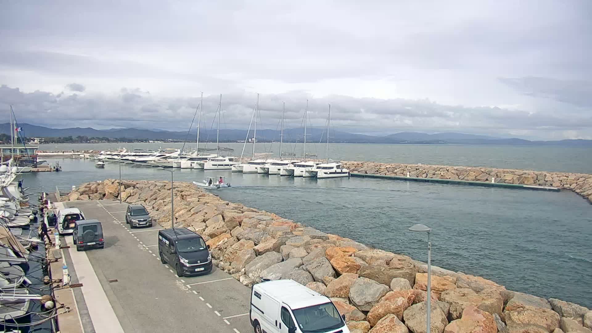 A marina with numerous sailboats and motorboats docked, surrounded by large rocks, under a cloudy sky.