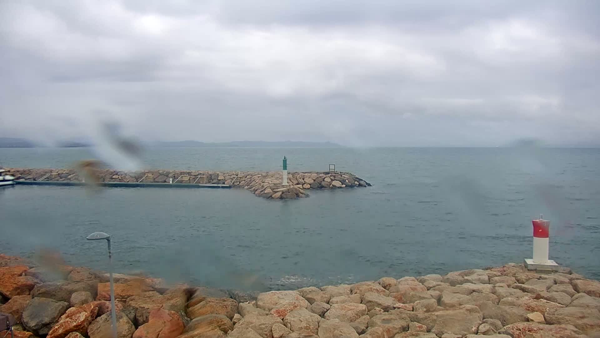 A rocky breakwater extends into a choppy sea under a cloudy, rainy sky.