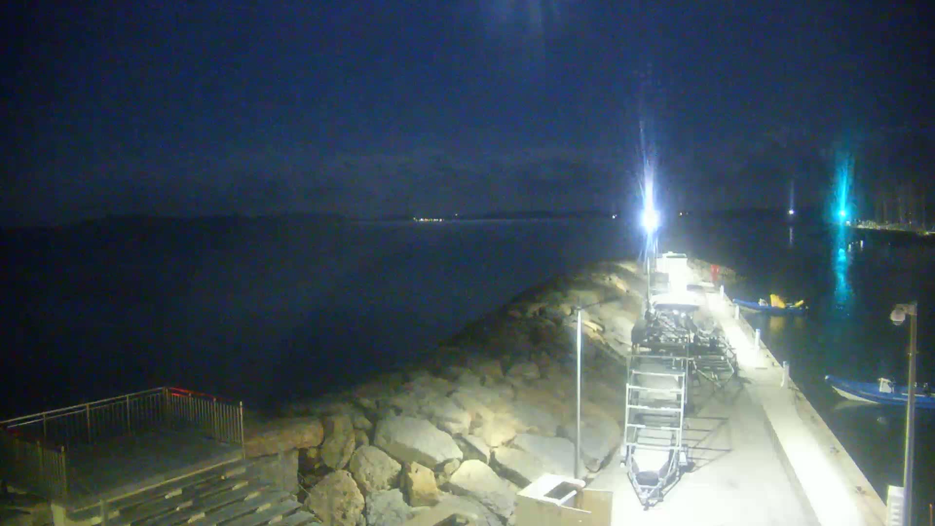 A nighttime view of a rocky shoreline with boats docked at a pier, under a dark, mostly clear sky.