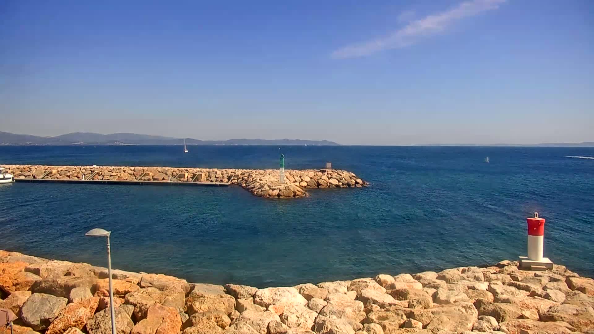 A rocky shoreline juts into a calm, blue sea under a clear, sunny sky, with a small boat visible in the distance.