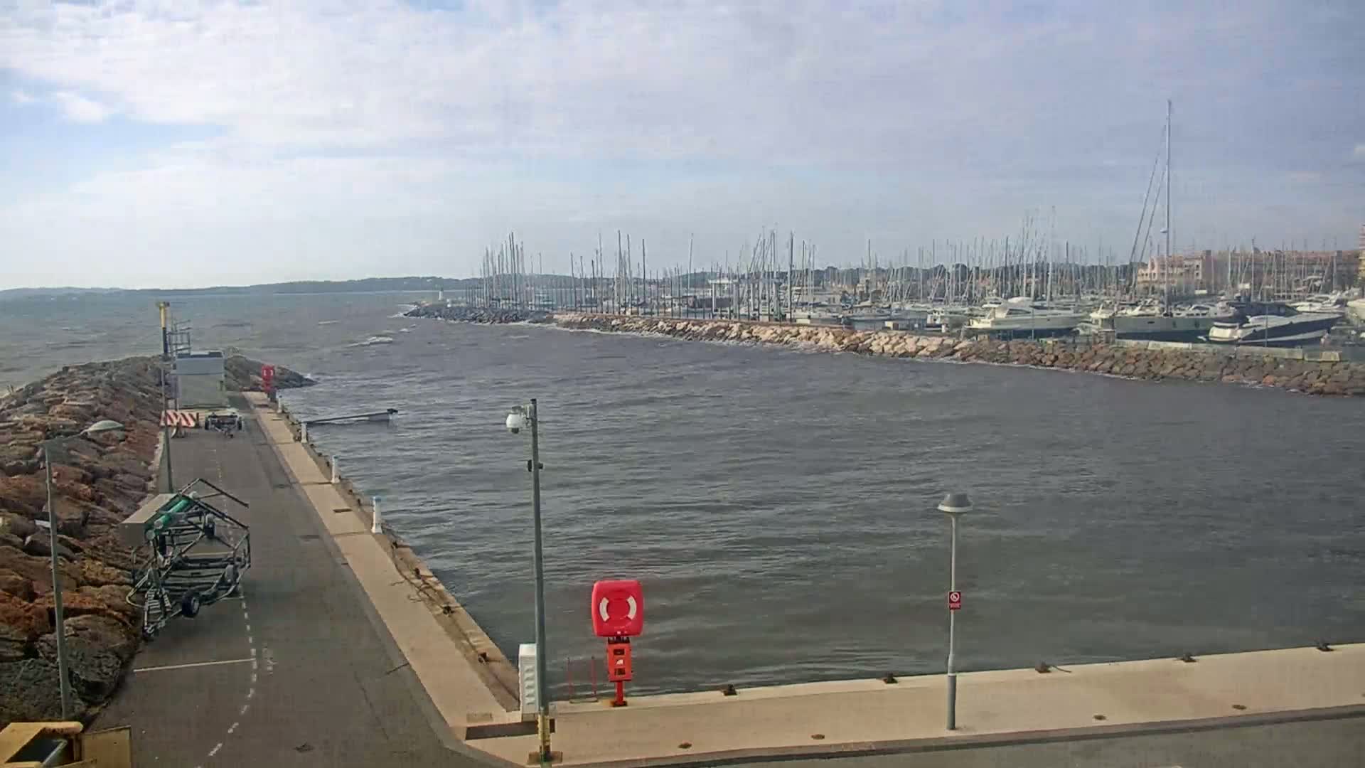A marina filled with numerous boats is visible across a choppy body of water, under a partly cloudy sky.