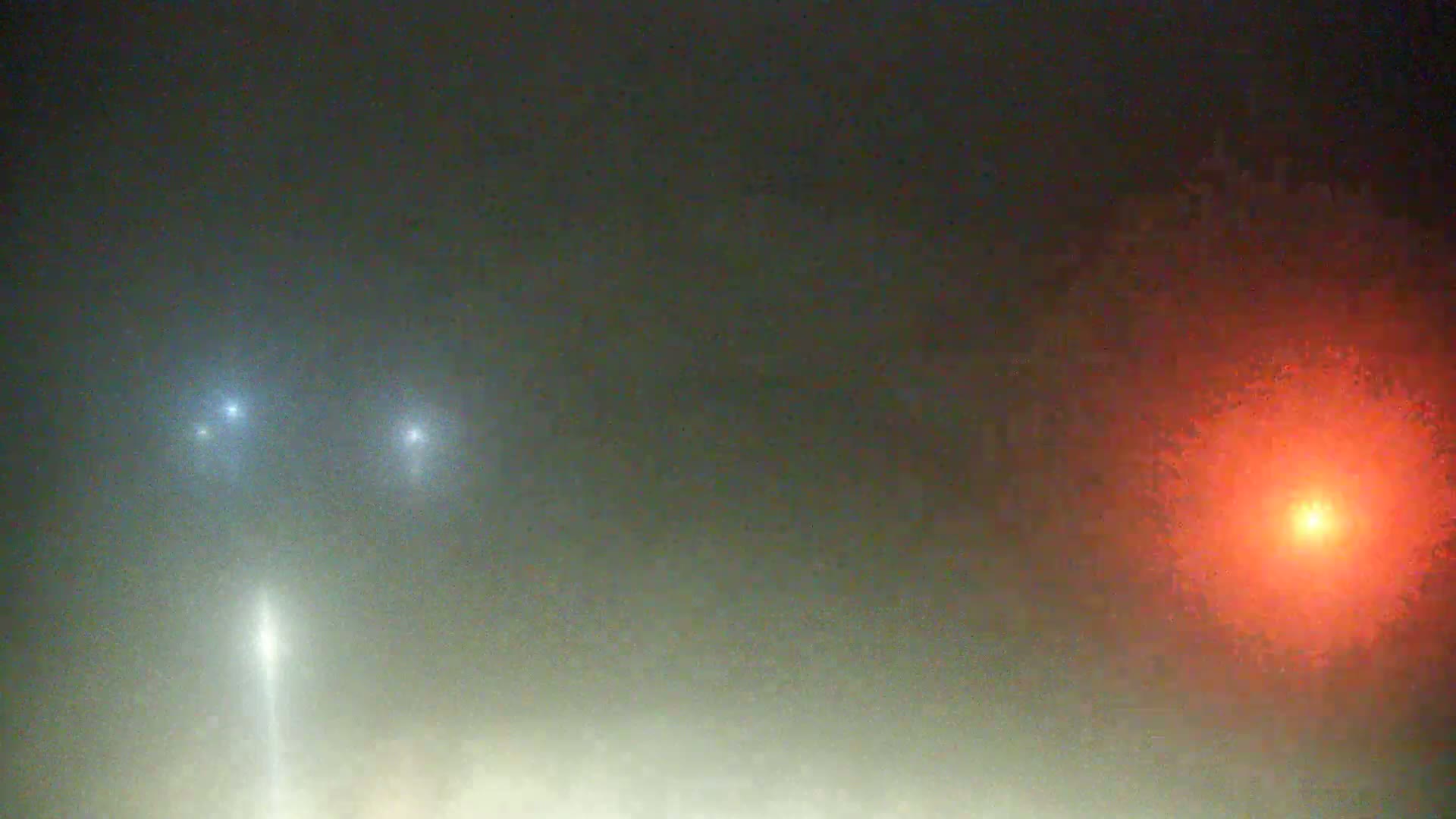 Two bluish lights and one reddish light are visible in a foggy night sky.