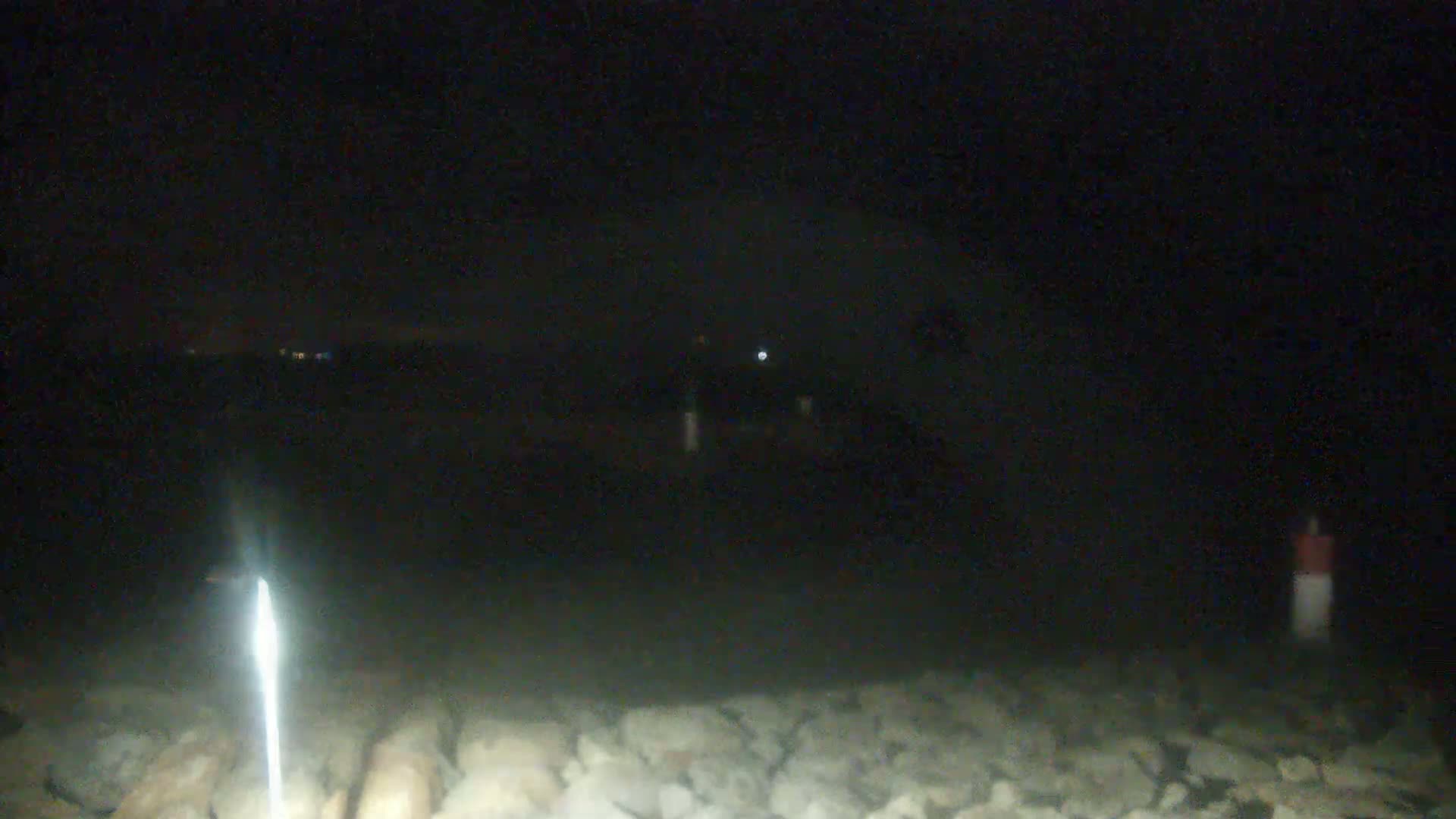 A bright light illuminates a rocky, dark shoreline at night.