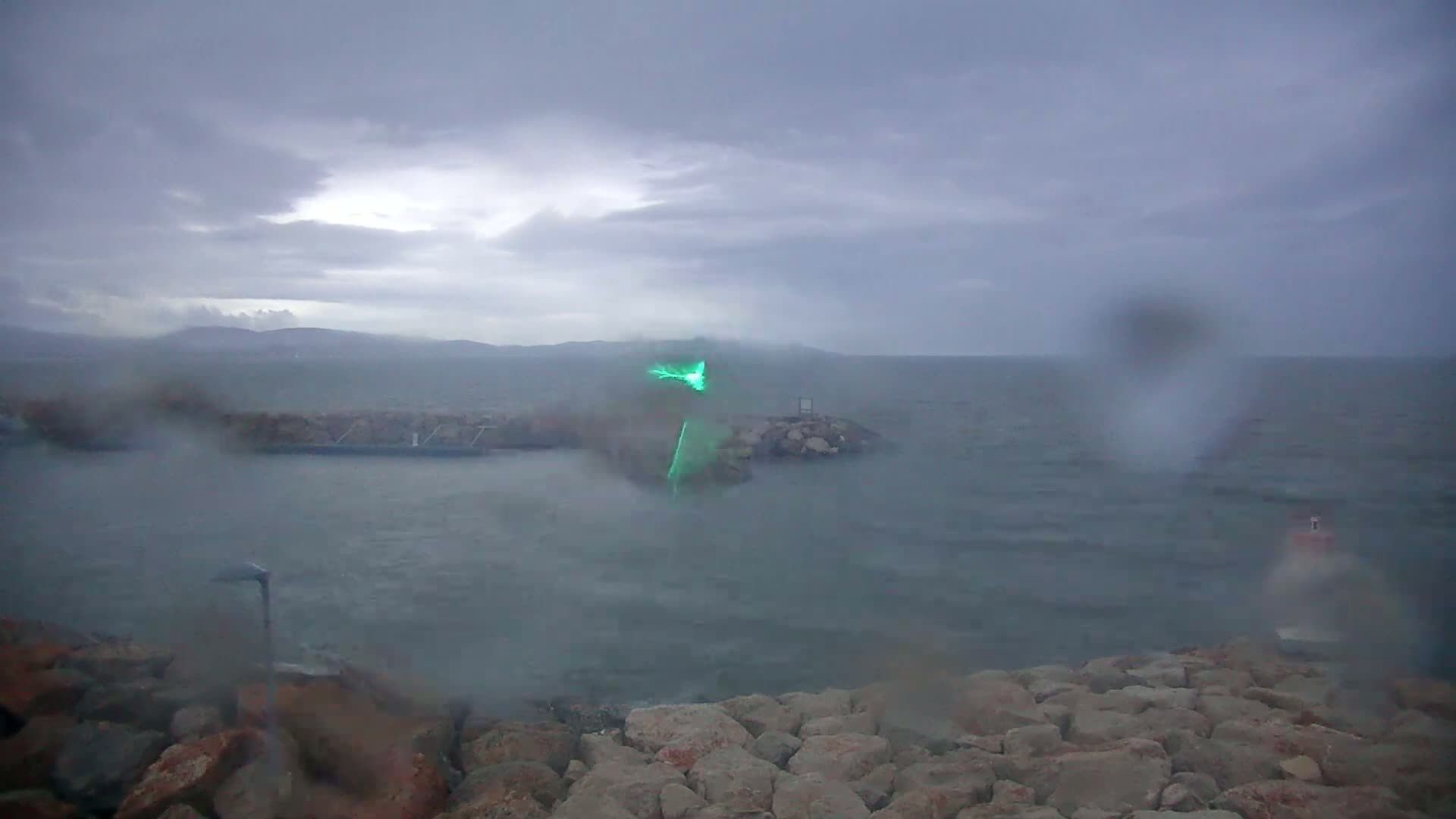 A rain-streaked view shows a choppy sea behind a rocky breakwater on an overcast day.