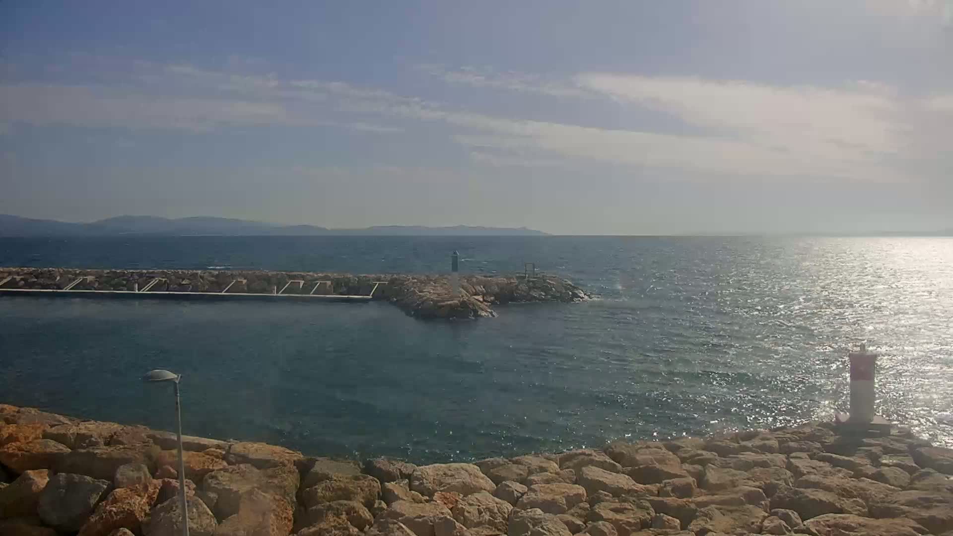 A rocky shoreline with a small harbor and a calm sea under a partly cloudy sky.