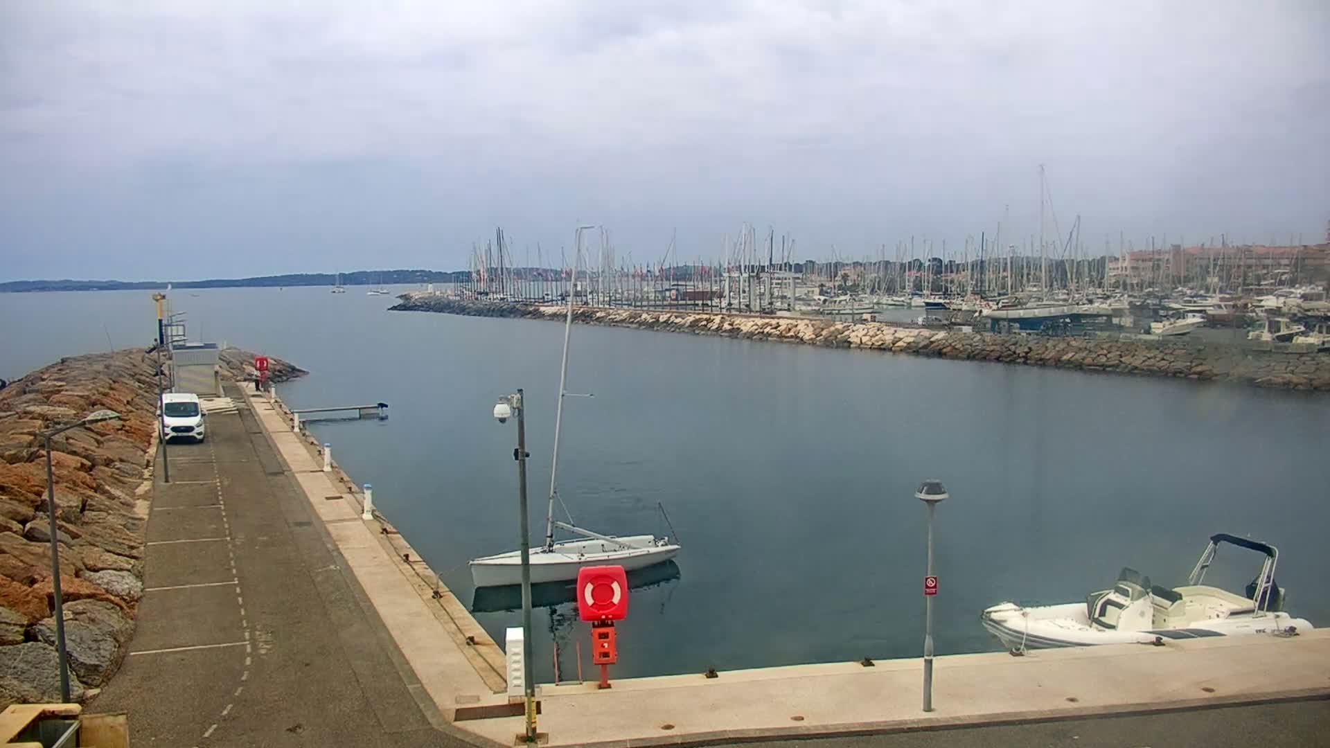 A marina filled with numerous boats on a cloudy day, with a small sailboat and motorboat docked at a nearby pier.
