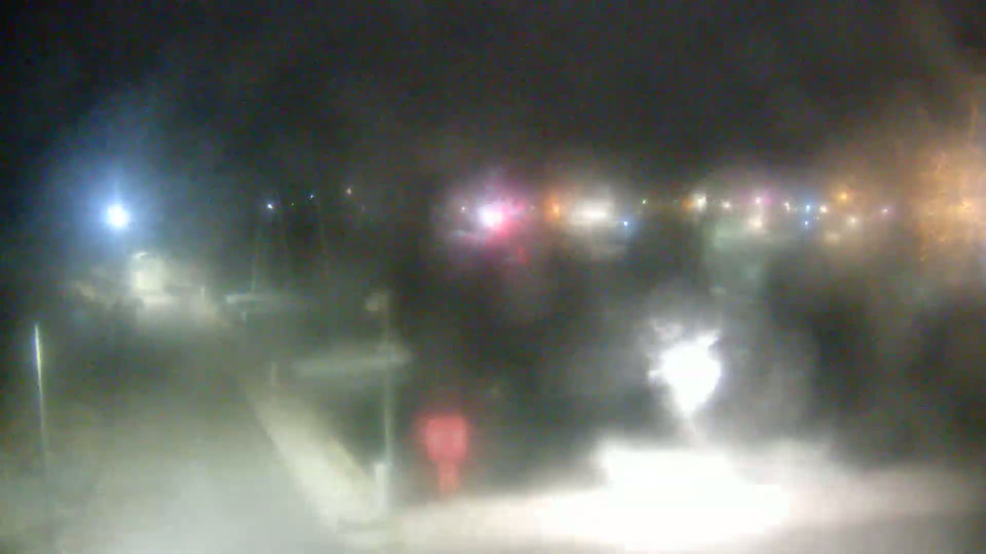 A blurry nighttime scene shows a road with indistinct vehicles and lights through heavy fog or mist.