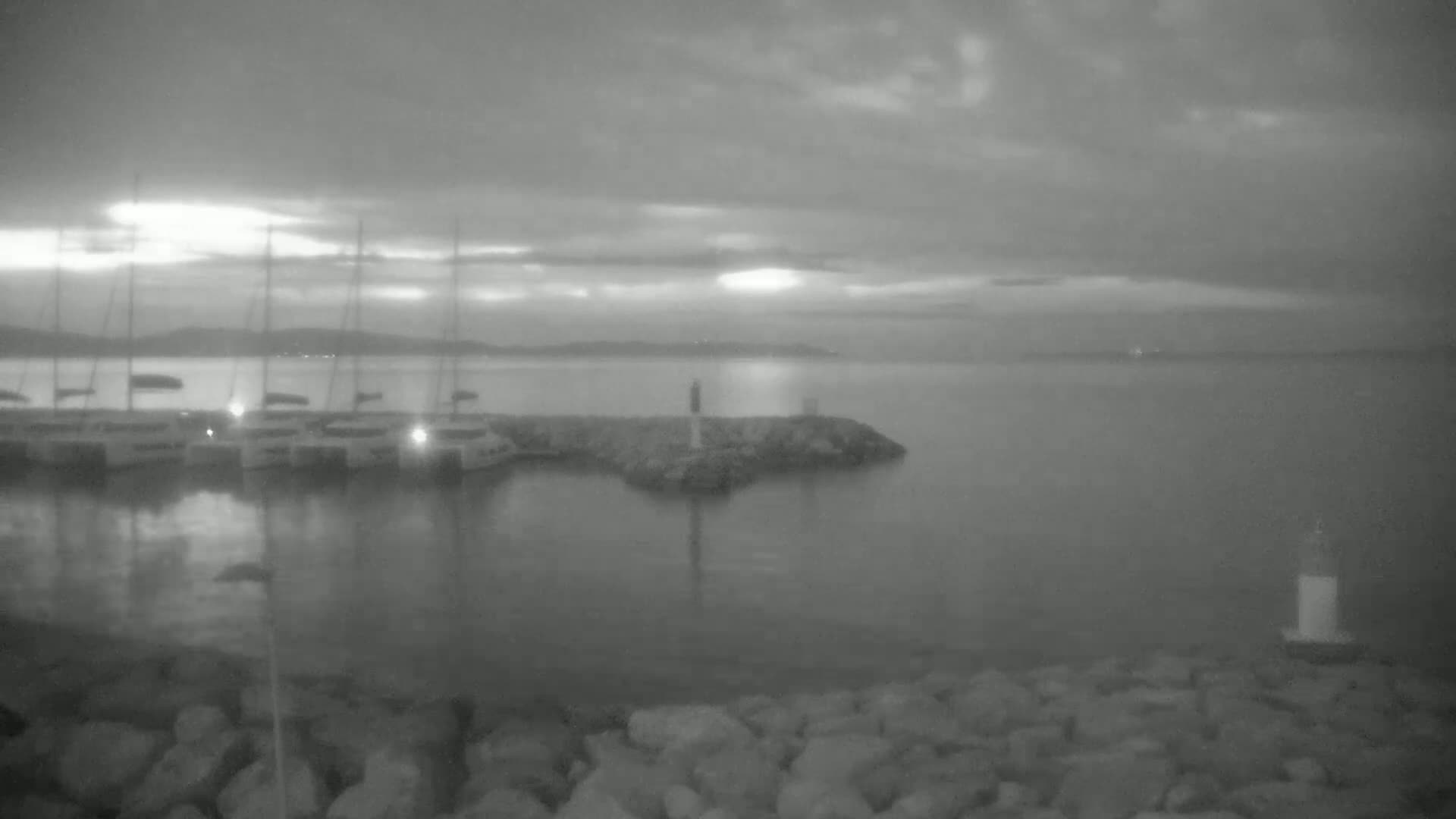 Several sailboats are moored in a harbor under a cloudy, twilight sky.