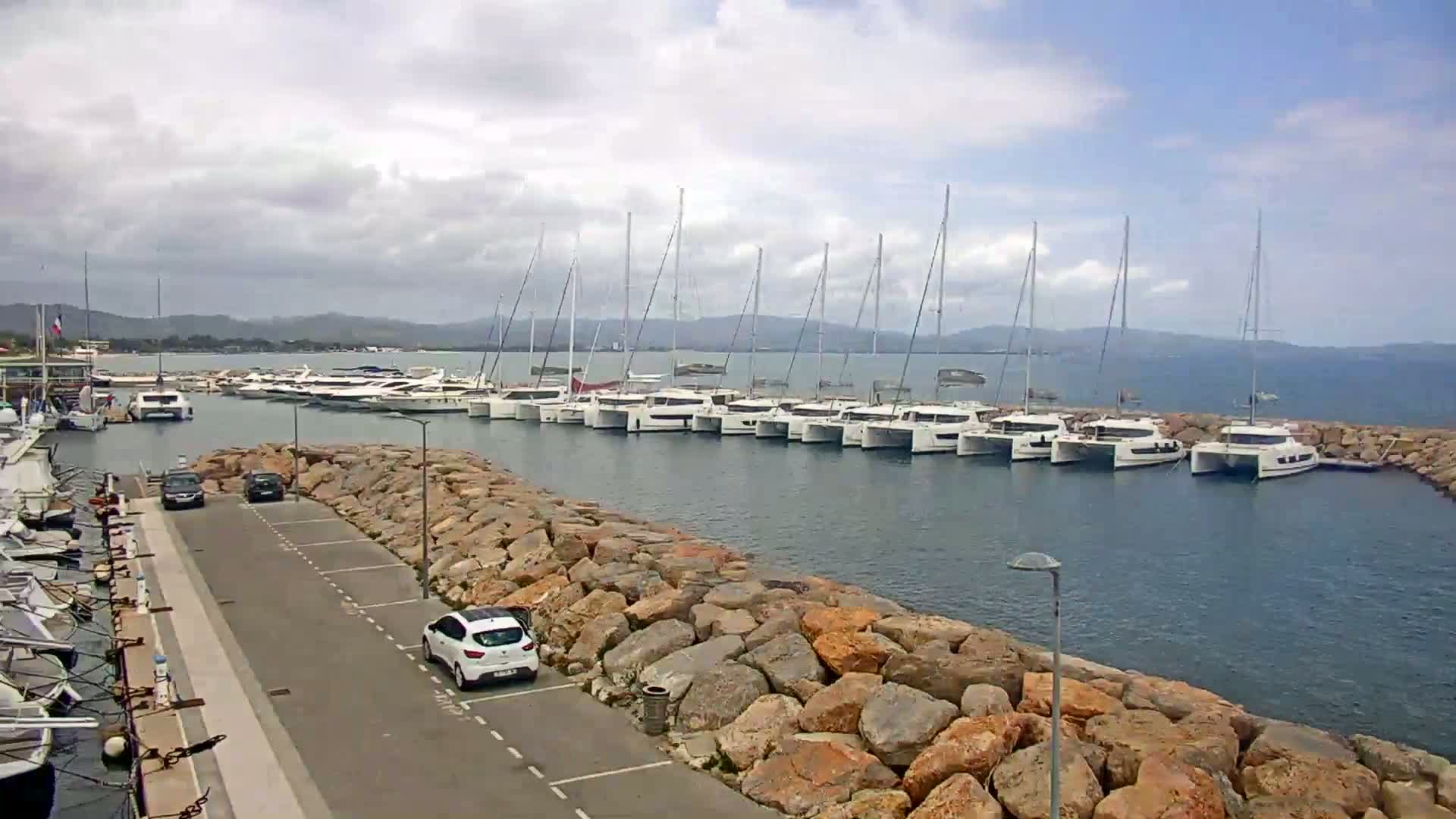 Many sailboats are docked in a marina on a partly cloudy day.