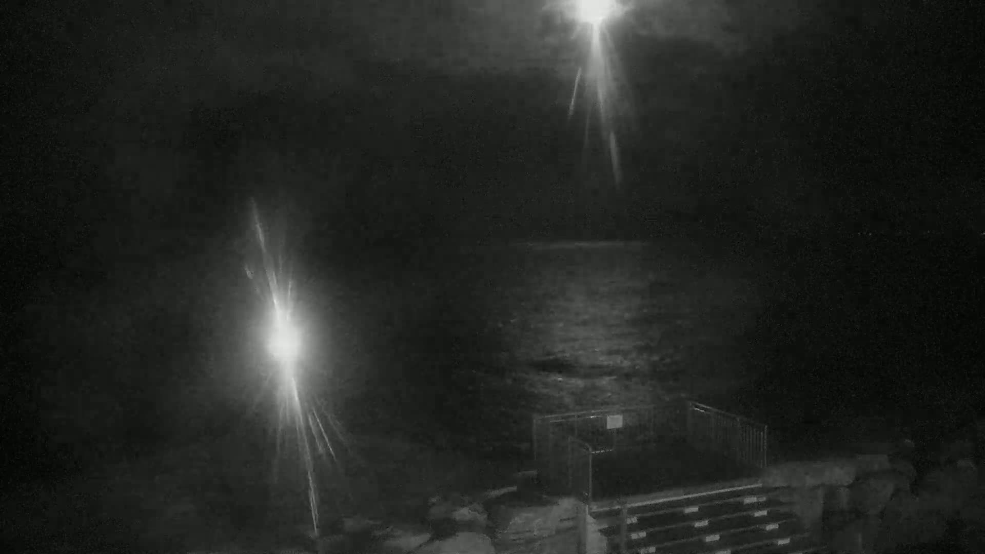 A nighttime, low-light view of a dark body of water, a metal structure, and bright light flares from unseen sources.