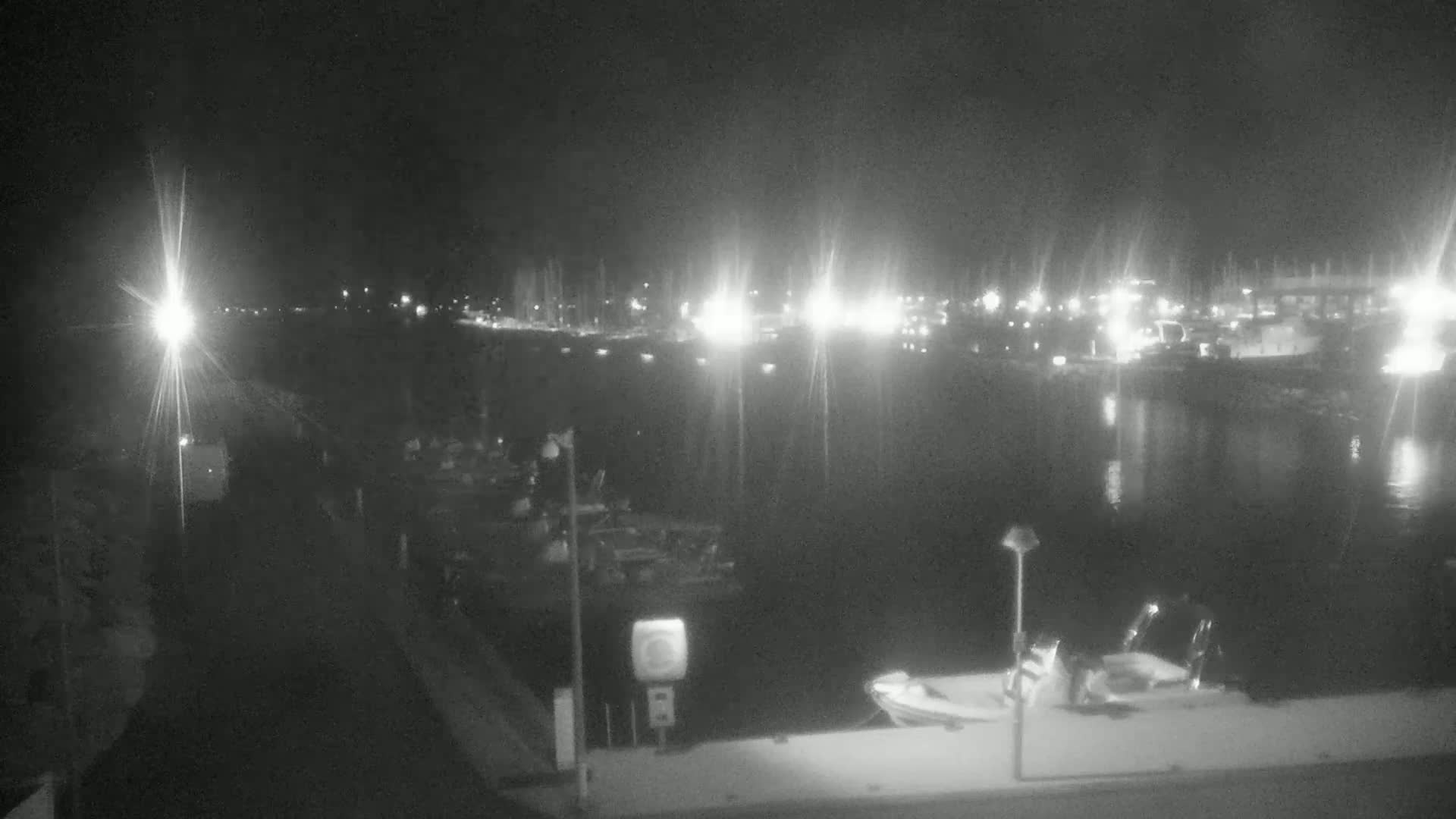 A nighttime view of a harbor with numerous boats and lights reflecting on the calm water.