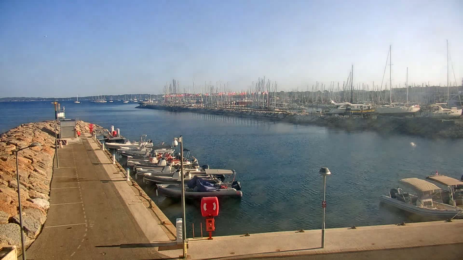 A marina with numerous boats and yachts docked along a seawall on a clear, sunny day.