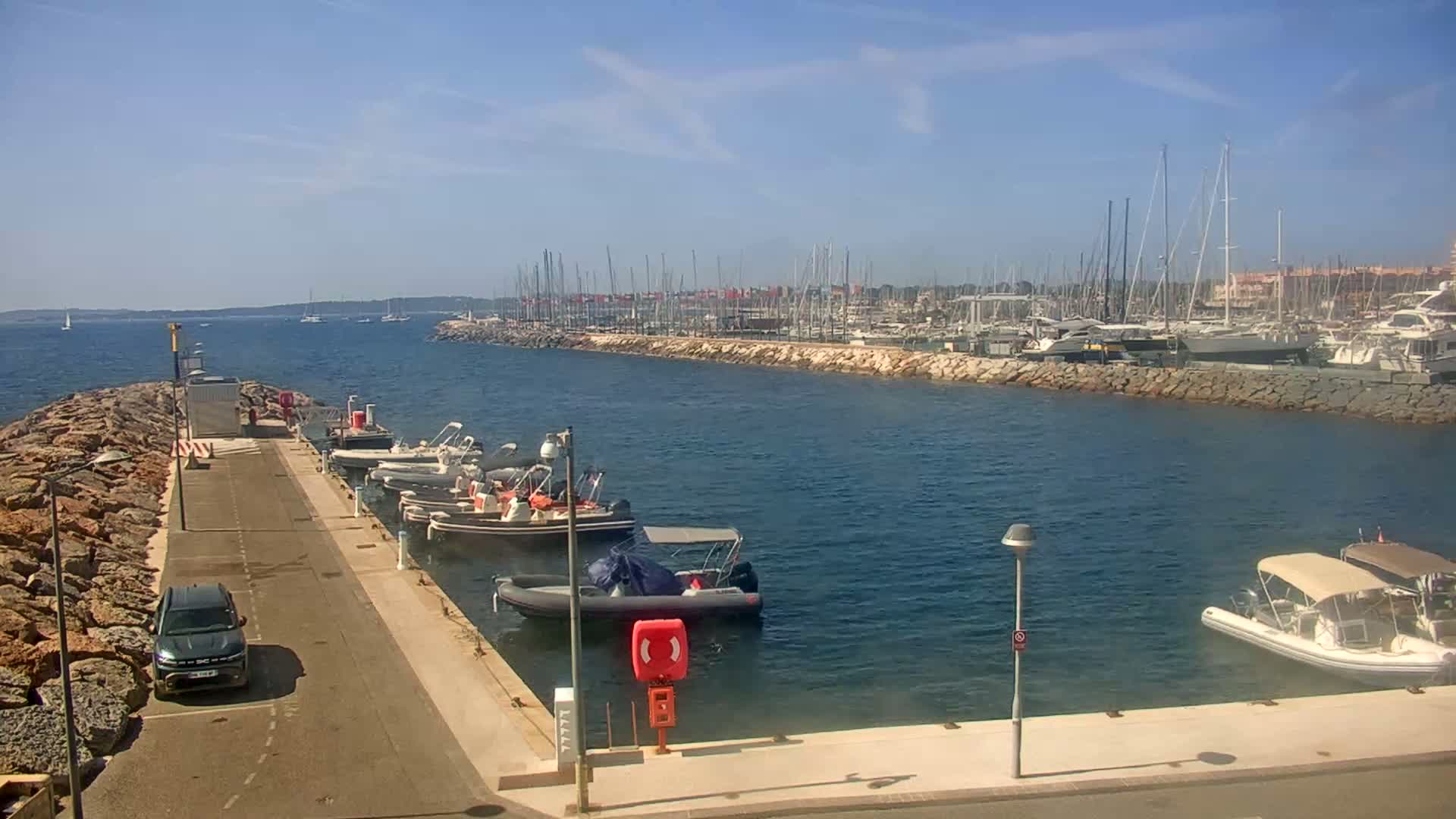 A marina filled with sailboats and motorboats on a sunny day, with a car parked near the dock.