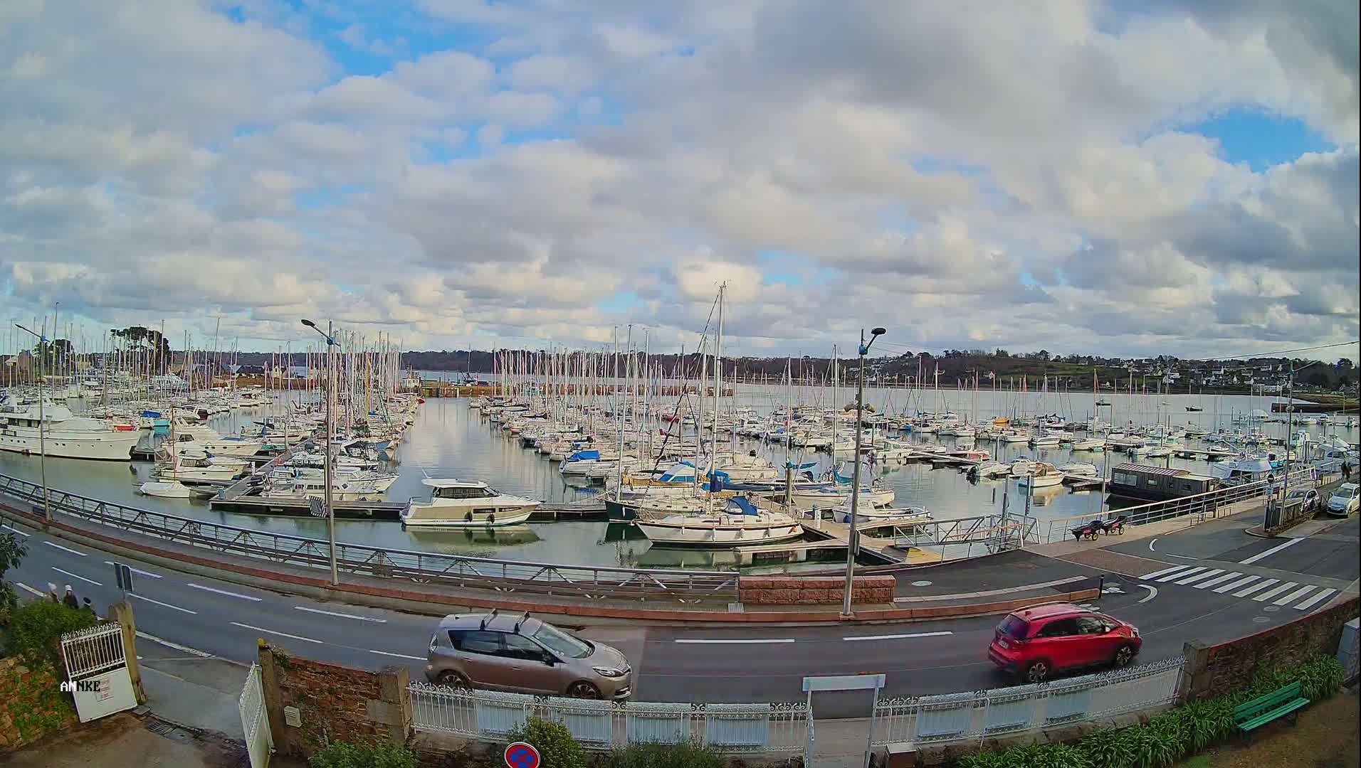 A marina filled with numerous boats is situated beside a road with a few cars under a partly cloudy sky.