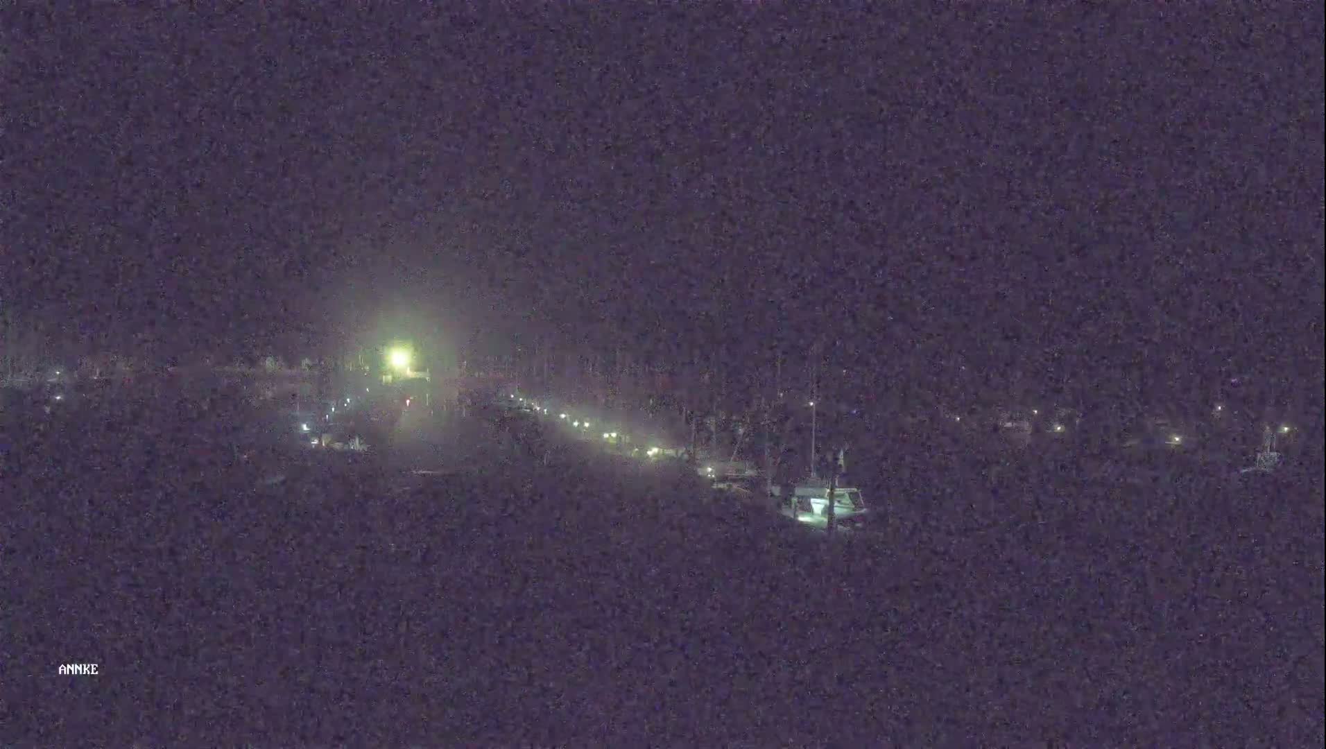 A dimly lit road at night shows vehicles driving toward a bright light in the distance.