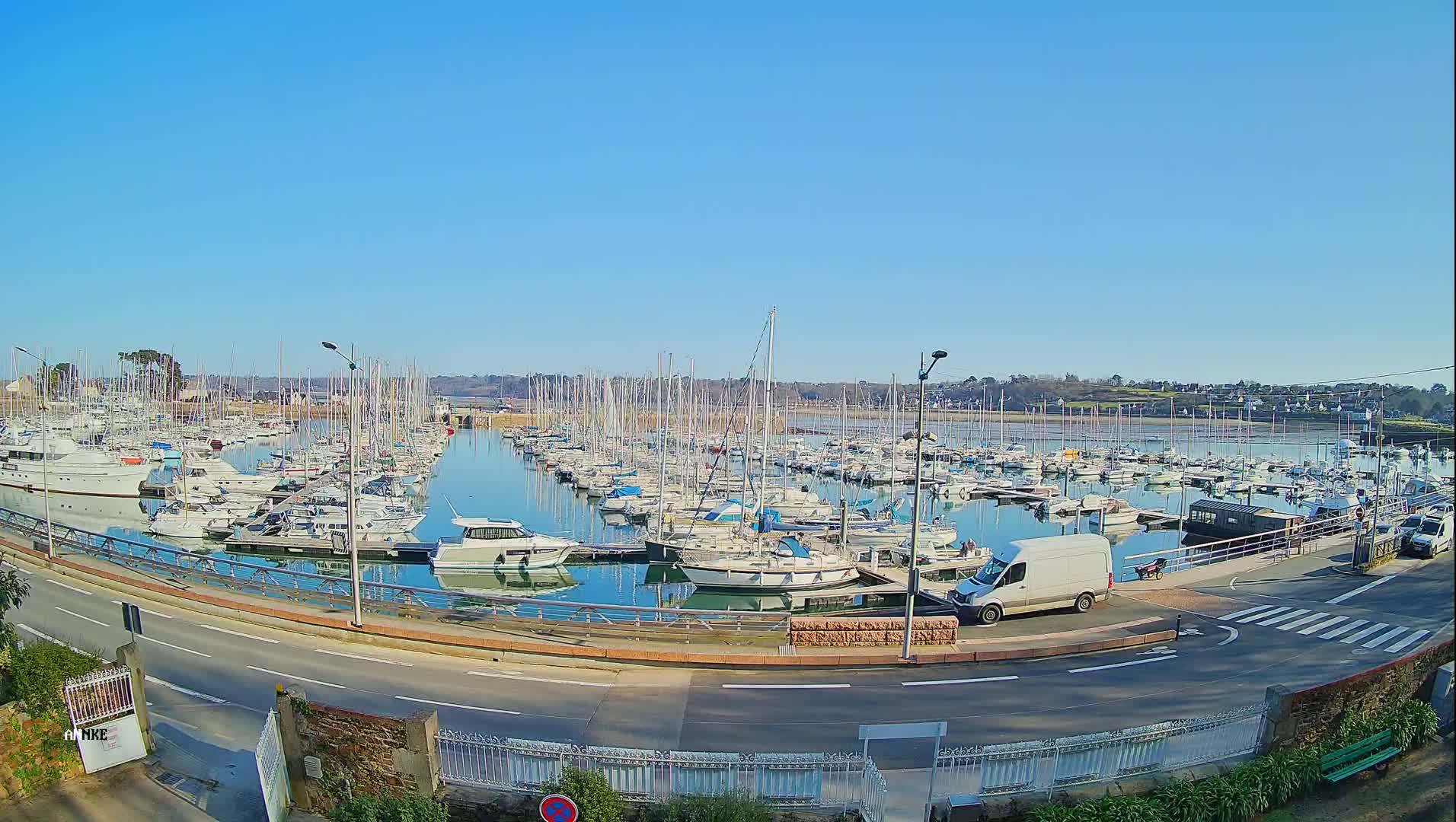 A sunny day reveals a marina filled with numerous sailboats and motorboats, docked along a calm body of water under a clear blue sky.