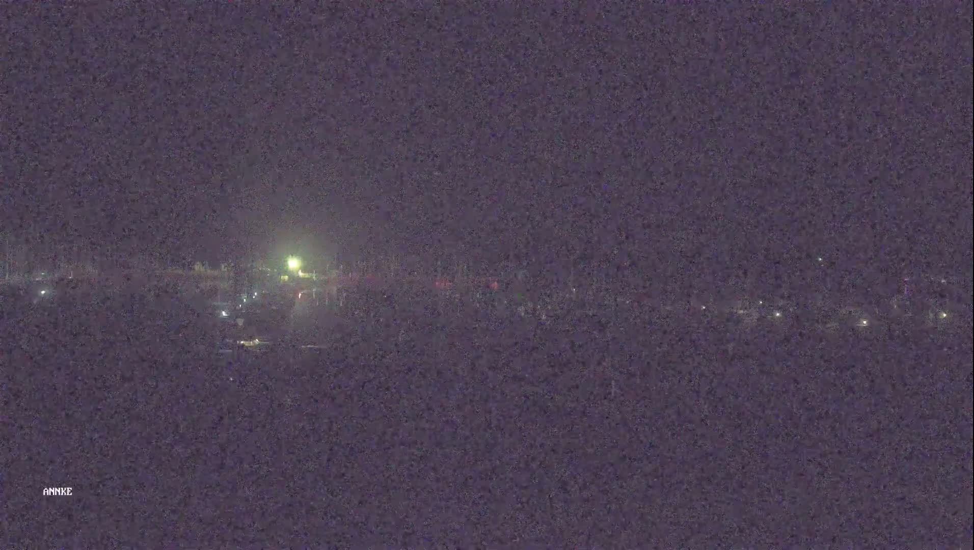 A nighttime long shot shows a dark landscape with a few scattered lights in the distance under a clear, dark sky.