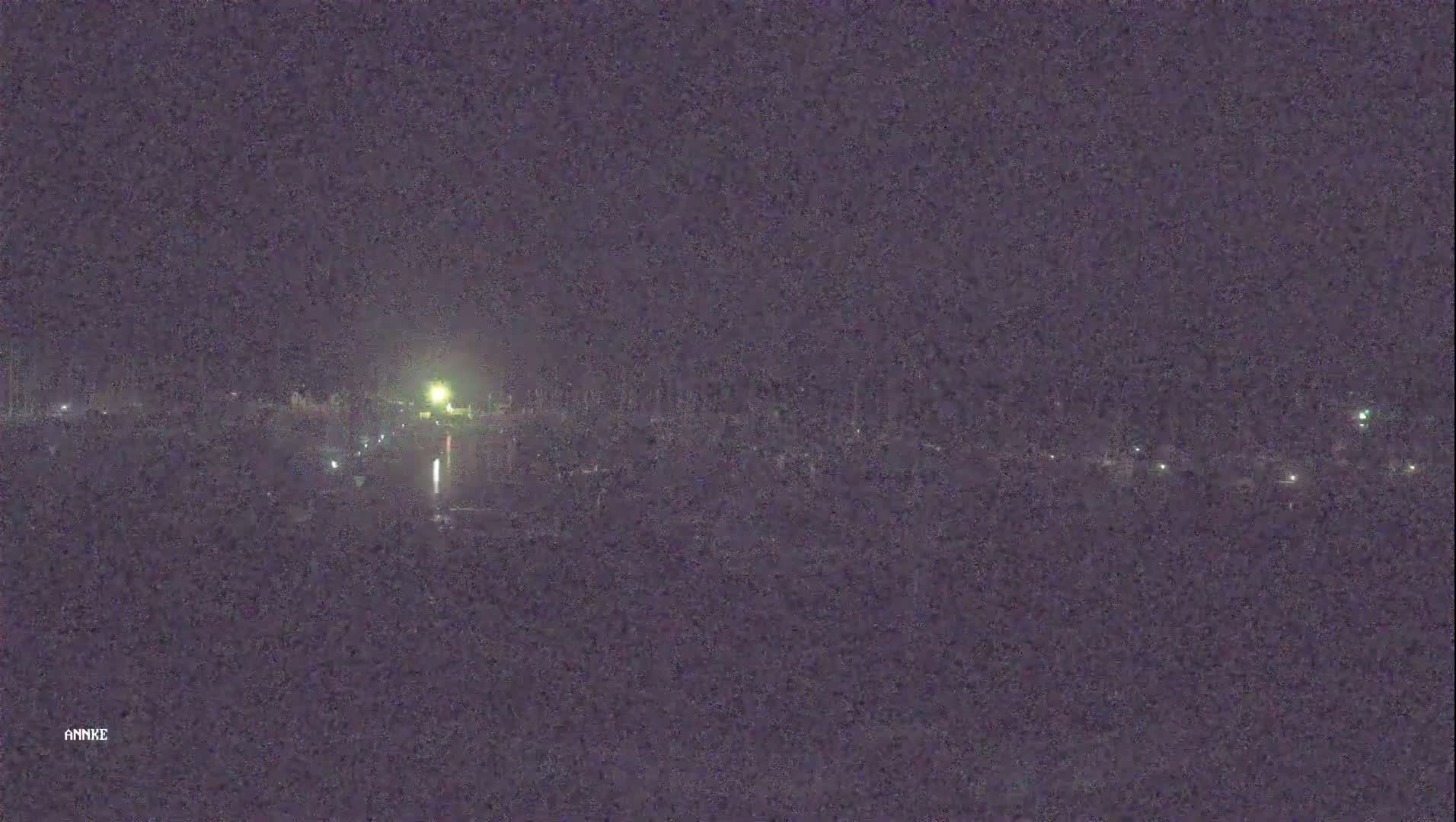 A nighttime long shot shows a dark landscape with a few distant lights and a bright light source in the center.