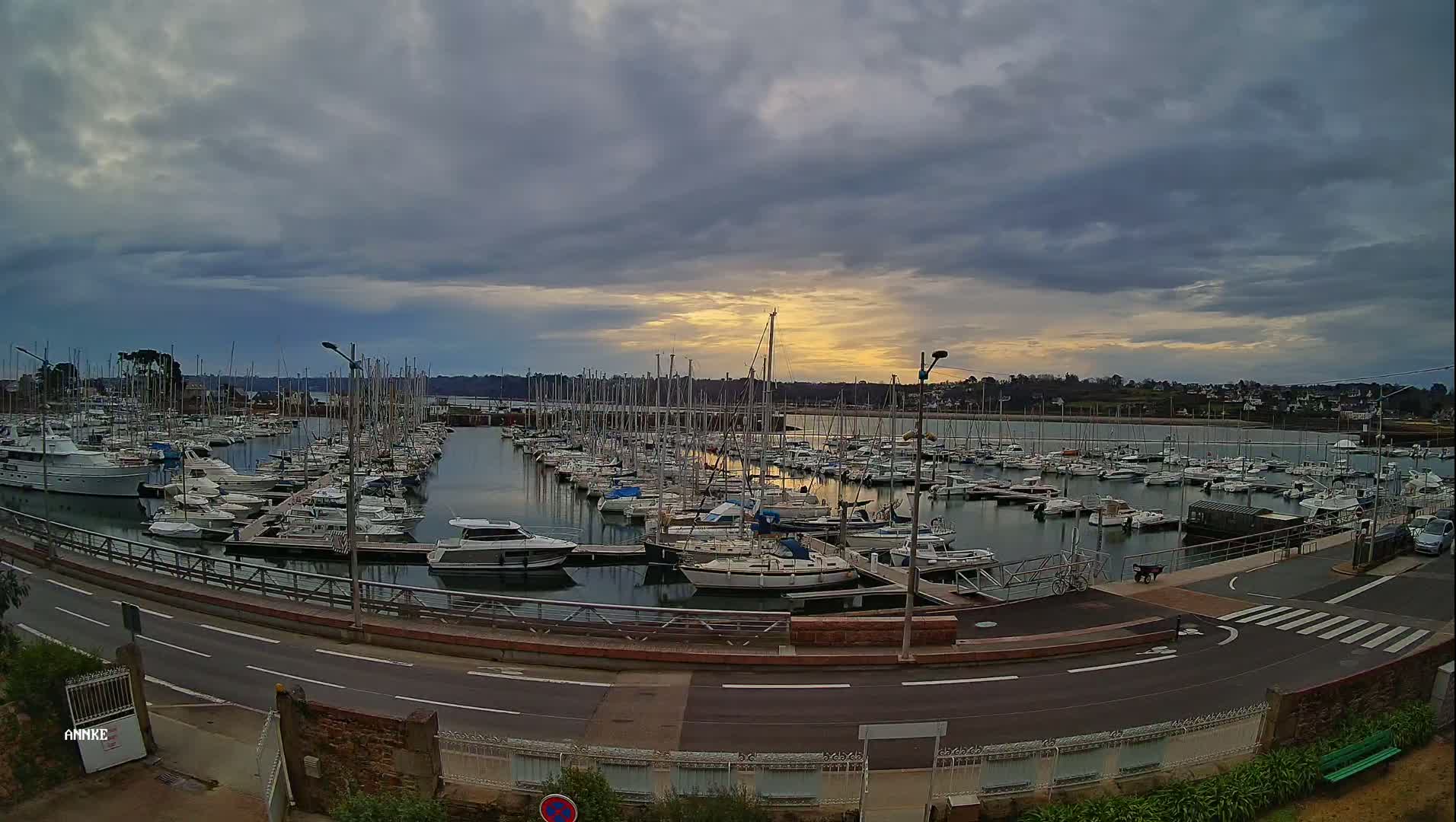 Many sailboats and motorboats are docked in a marina under a partly cloudy sky, with a hint of sunset visible.
