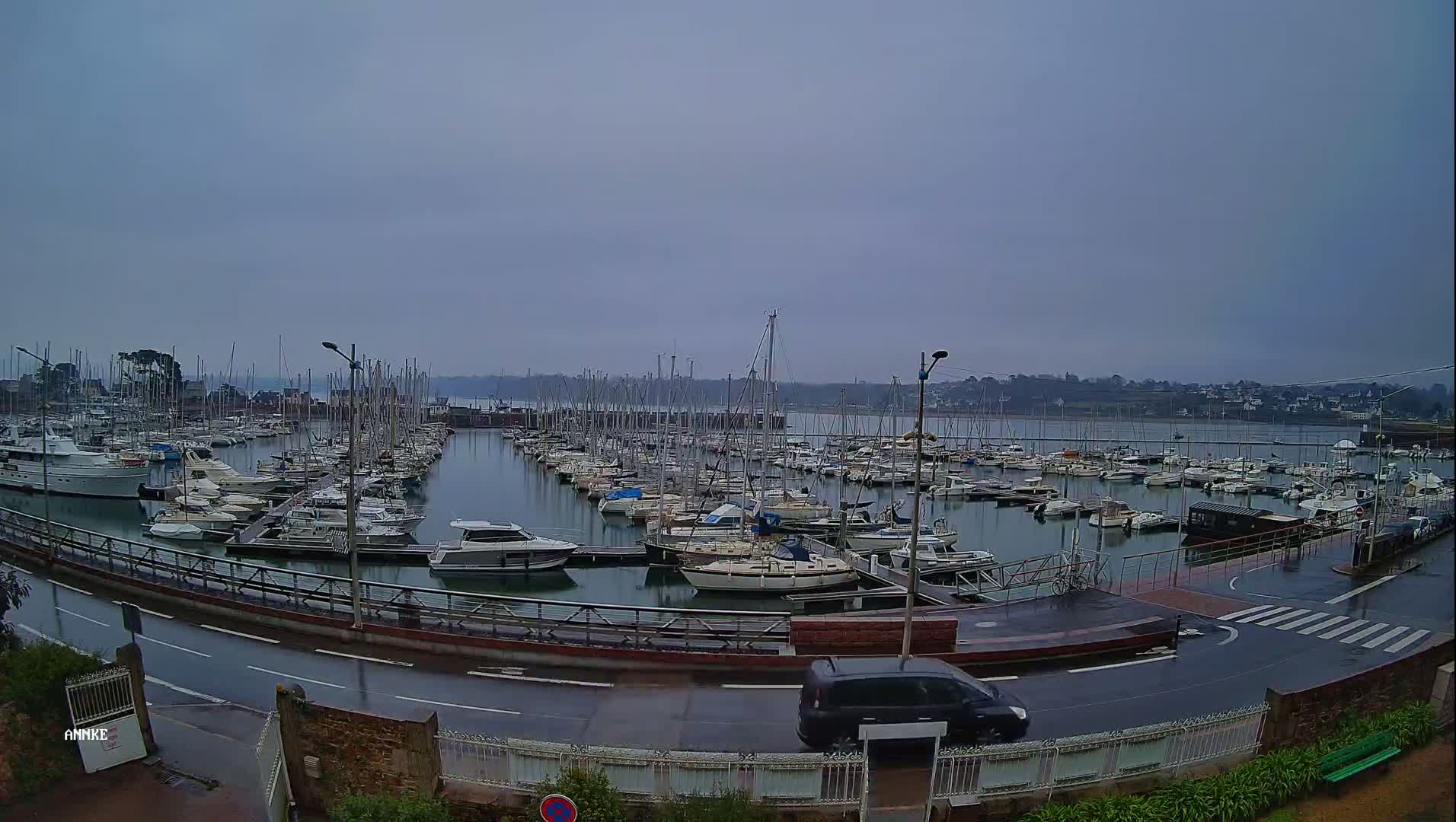 A marina filled with numerous sailboats and motorboats is seen on an overcast, rainy day.