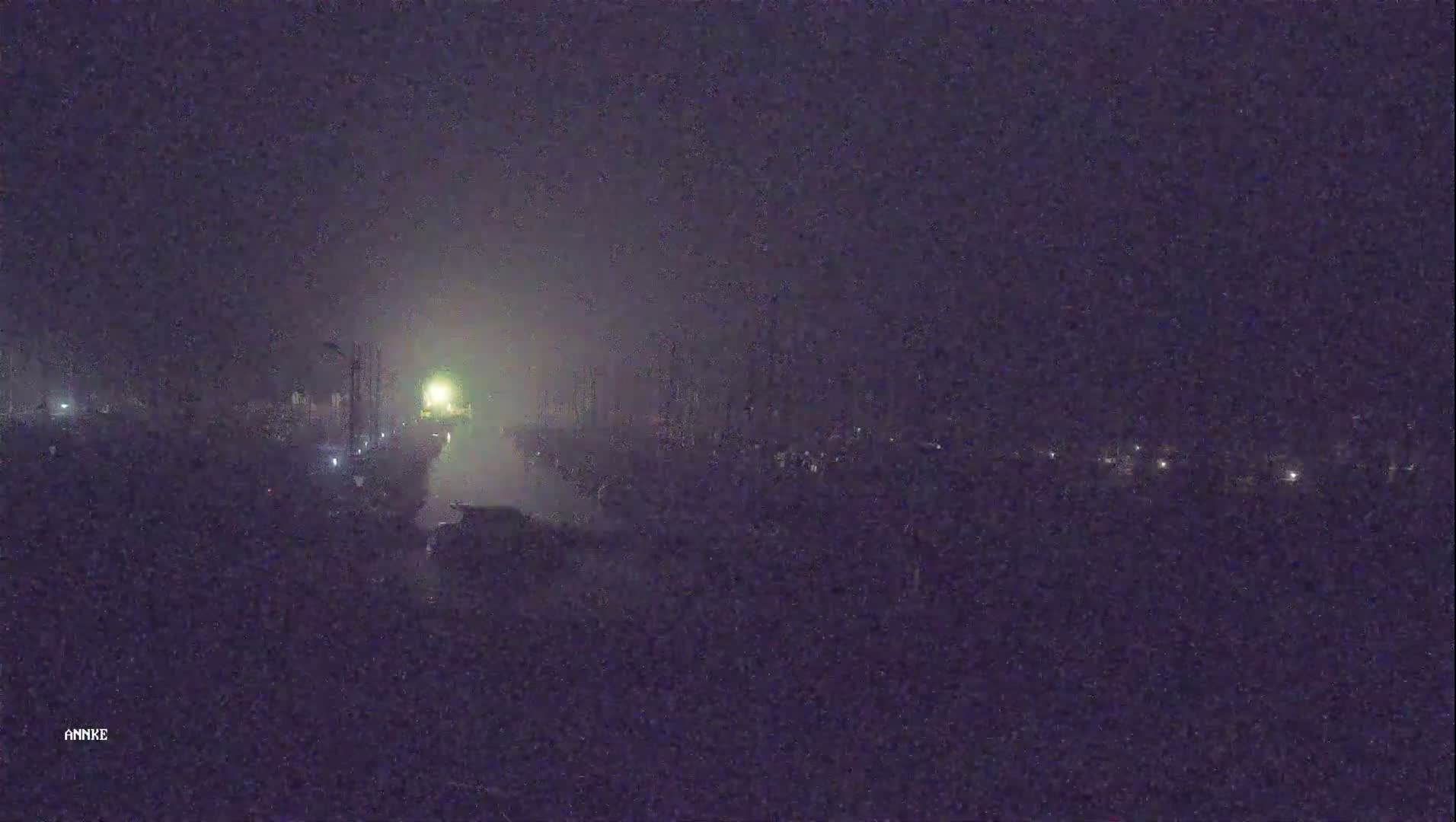 A hazy, nighttime view shows a dimly lit road with vehicles and faint lights in the distance.