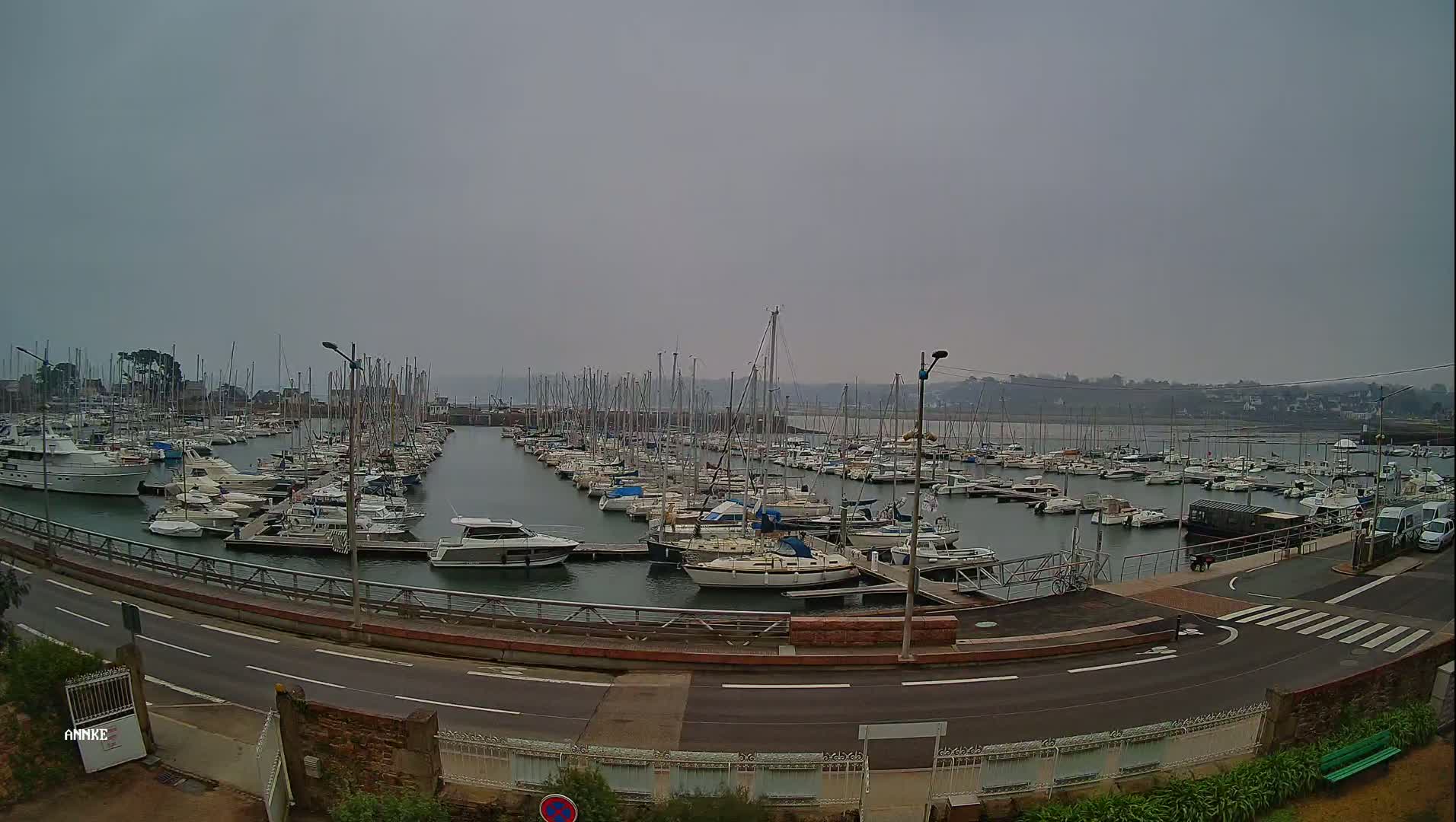 A marina filled with numerous sailboats and motorboats is visible on an overcast day.