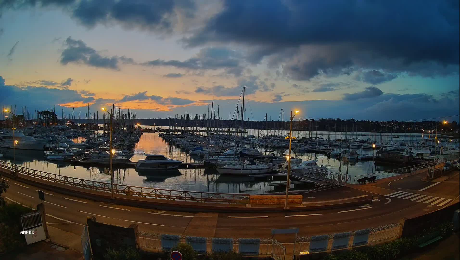 Many sailboats are docked in a marina at sunset under a partly cloudy sky.