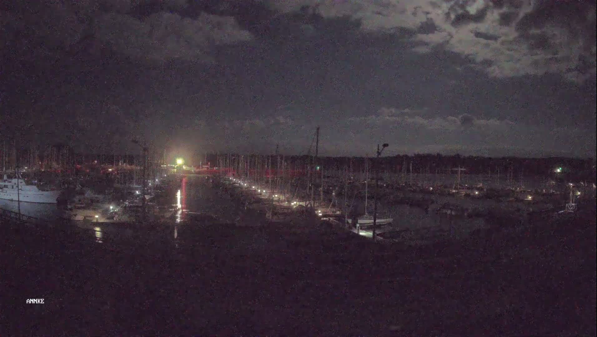 A nighttime view of a marina filled with boats under a partly cloudy sky.