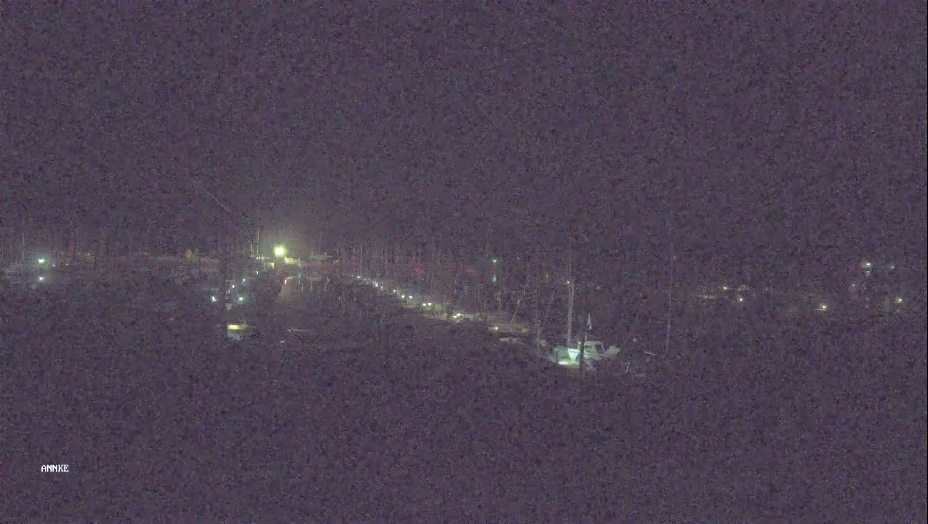 A long, dimly lit road at night is lined with docked boats, under a dark sky.