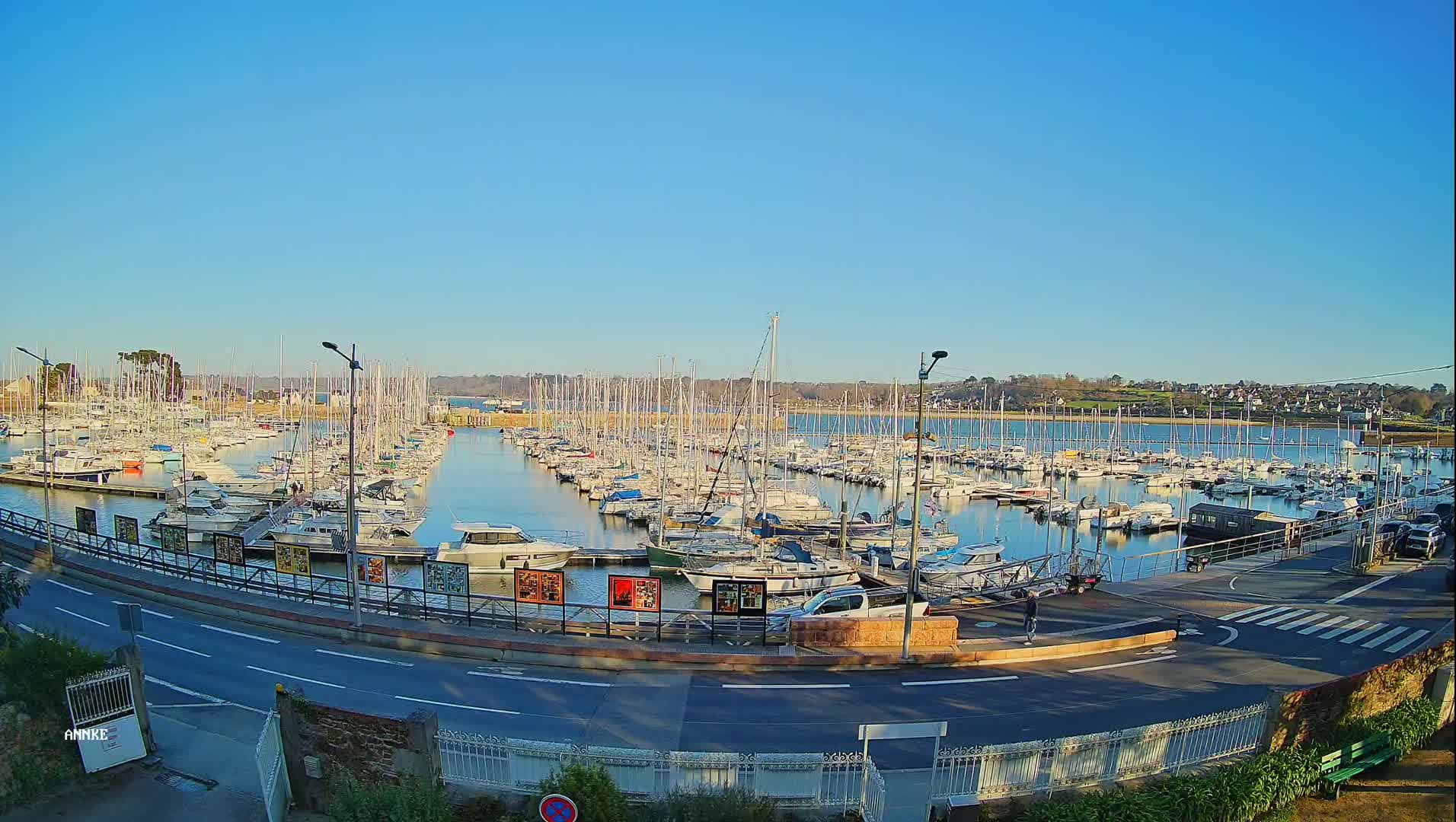 A large marina filled with numerous sailboats and motorboats is seen on a clear, sunny day.