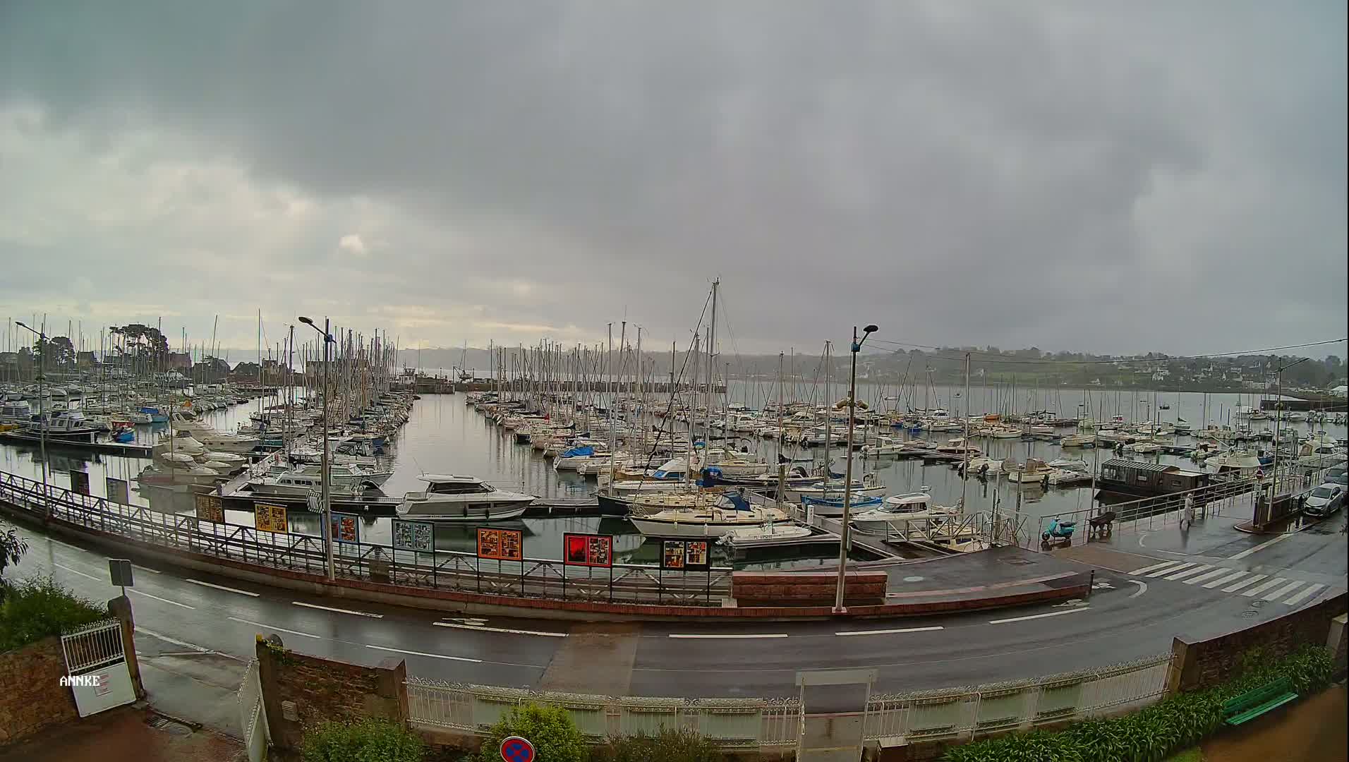 Many sailboats and motorboats are docked in a marina on an overcast, rainy day.