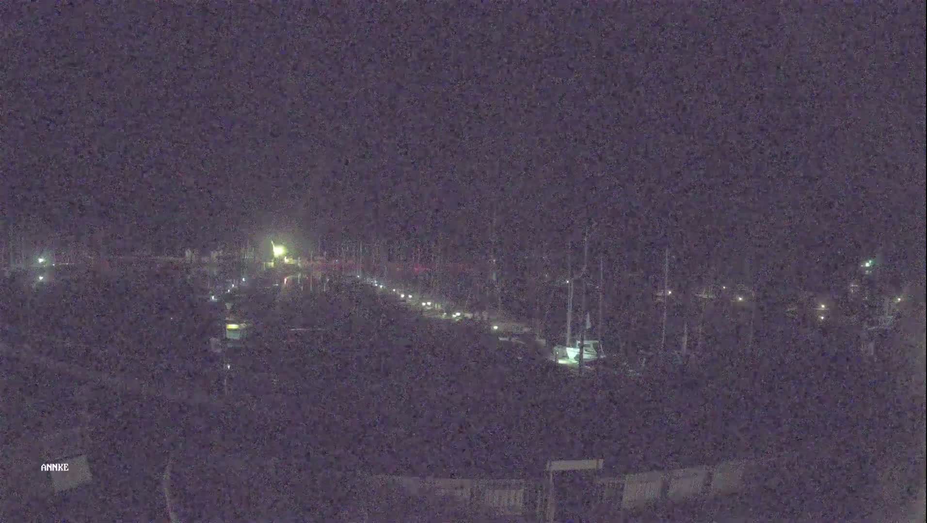 A nighttime long shot shows a marina with boats docked, illuminated by faint lights under a dark sky.
