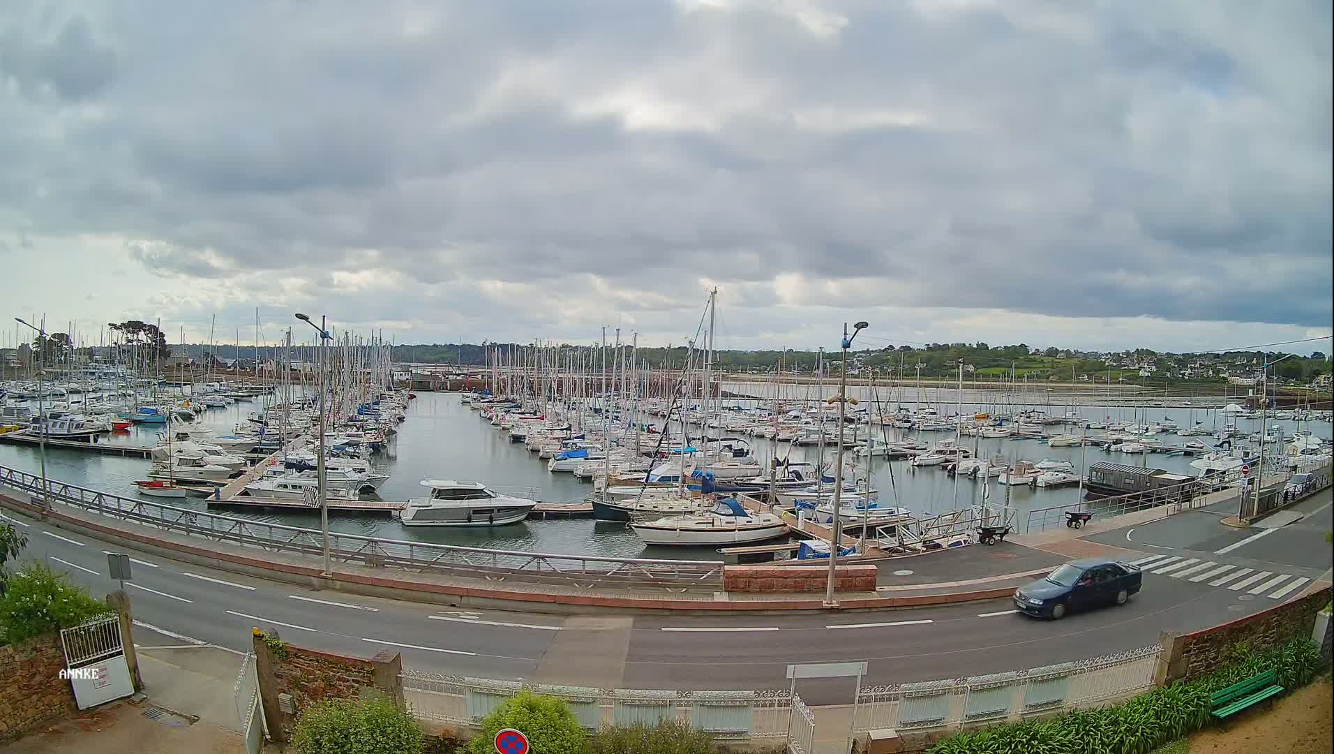 A marina filled with numerous sailboats and motorboats is viewed from a slightly elevated vantage point under an overcast sky.