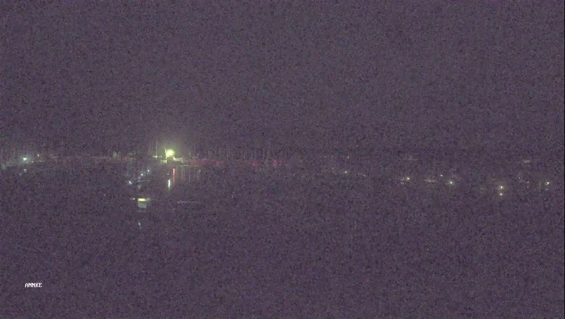 A nighttime, low-light view shows a dark body of water reflecting a few faint lights from what appears to be a distant shoreline.
