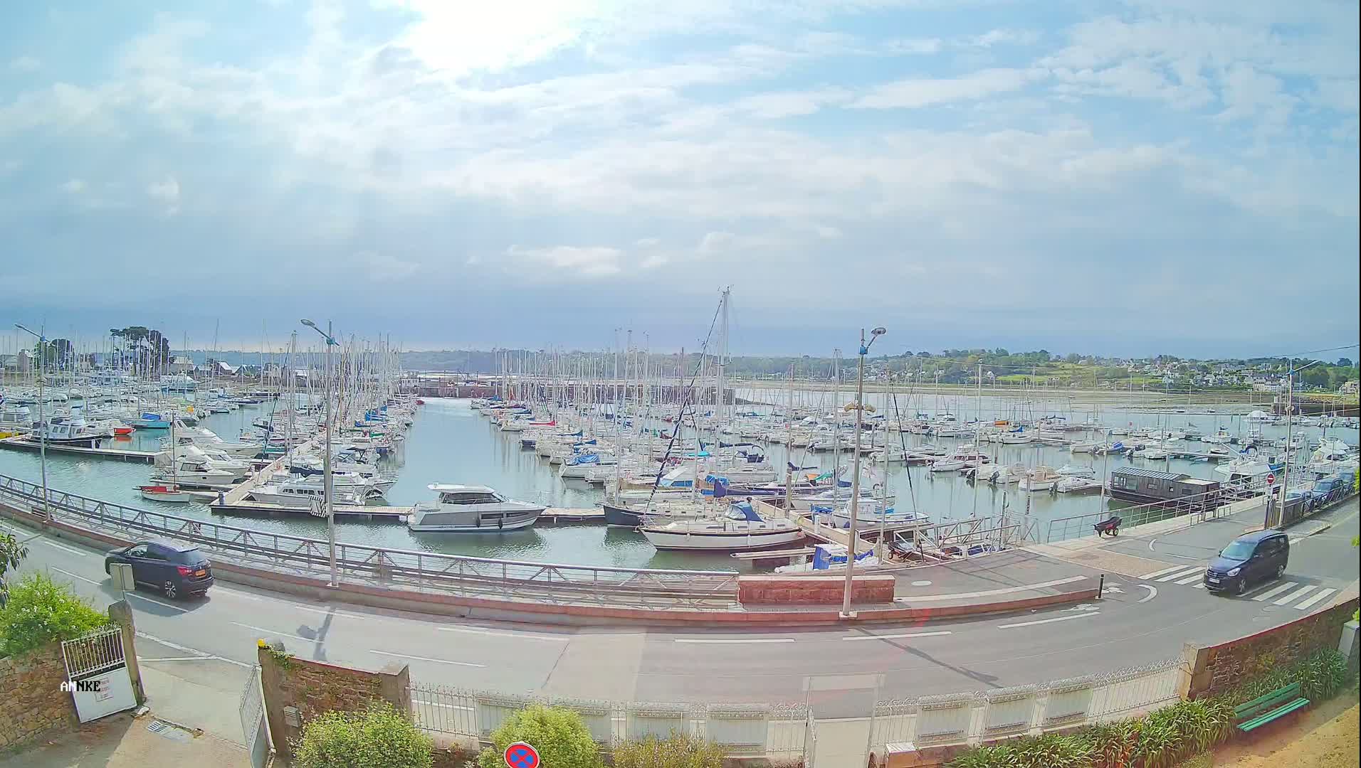 A marina filled with numerous sailboats and motorboats is visible under a partly cloudy sky.