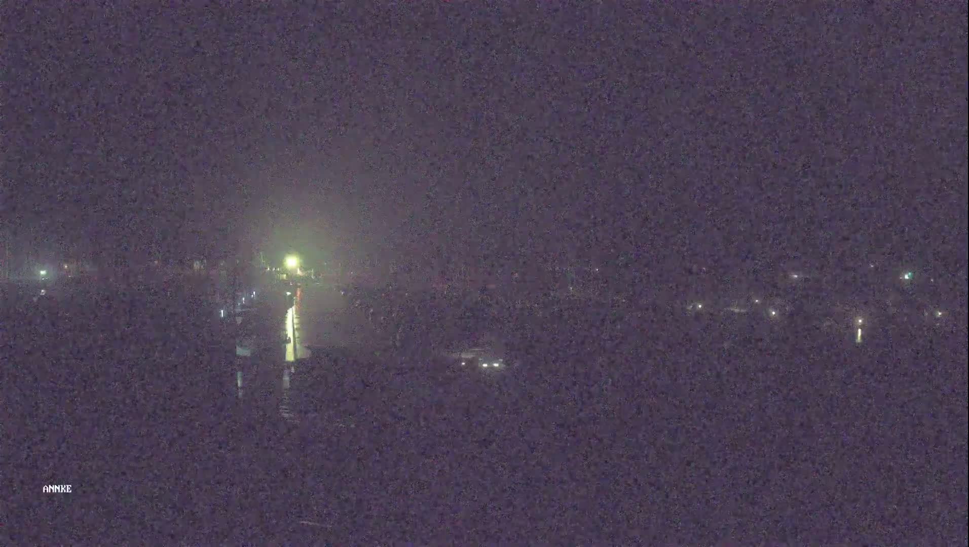 A nighttime, low-light view of a waterway with dimly lit buildings and vehicles along its edges.