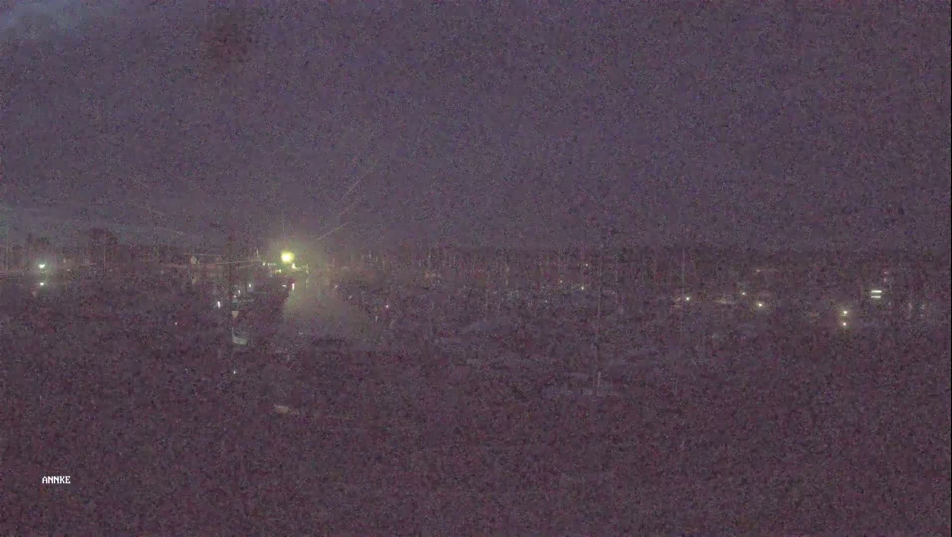 A nighttime view of a marina under a dark, possibly stormy sky shows numerous boats and lights along a waterway.