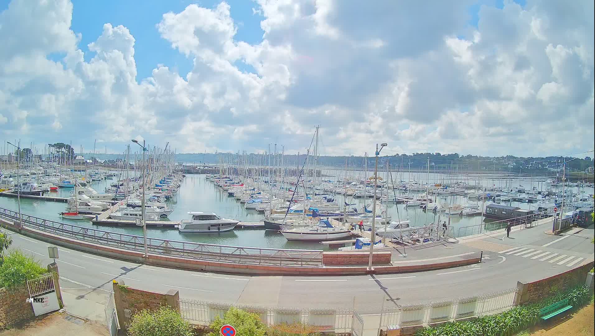 A large marina filled with numerous sailboats and motorboats is seen under a partly cloudy sky.