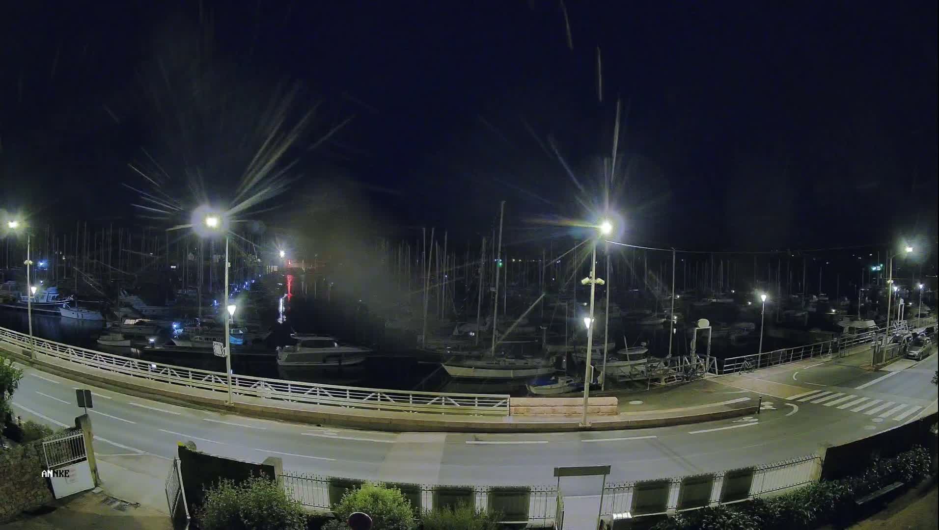A nighttime, high-angle view of a marina filled with numerous boats docked under a dark sky with some light rain or spray.