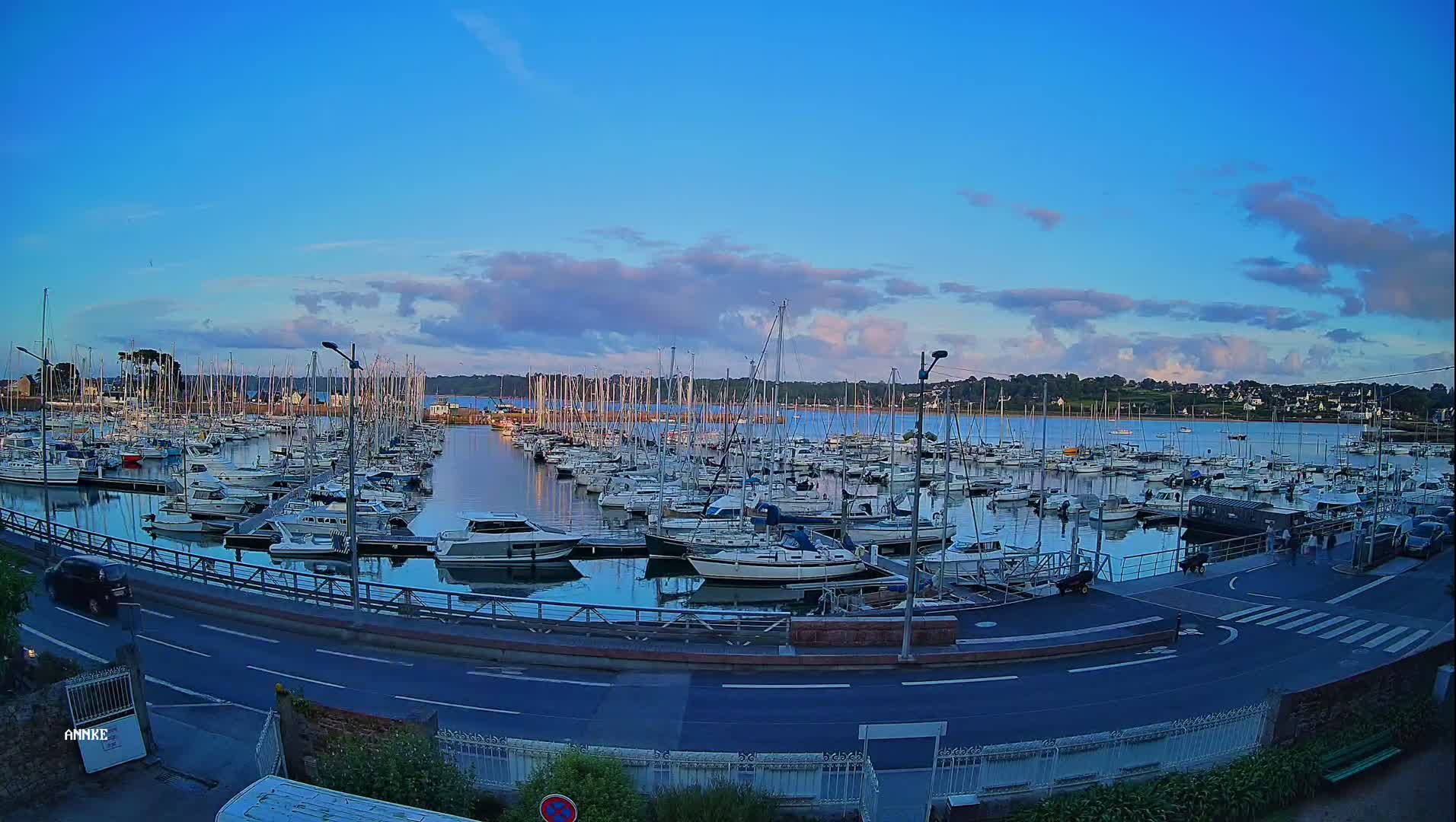 A marina filled with numerous sailboats and motorboats under a partly cloudy, twilight sky.