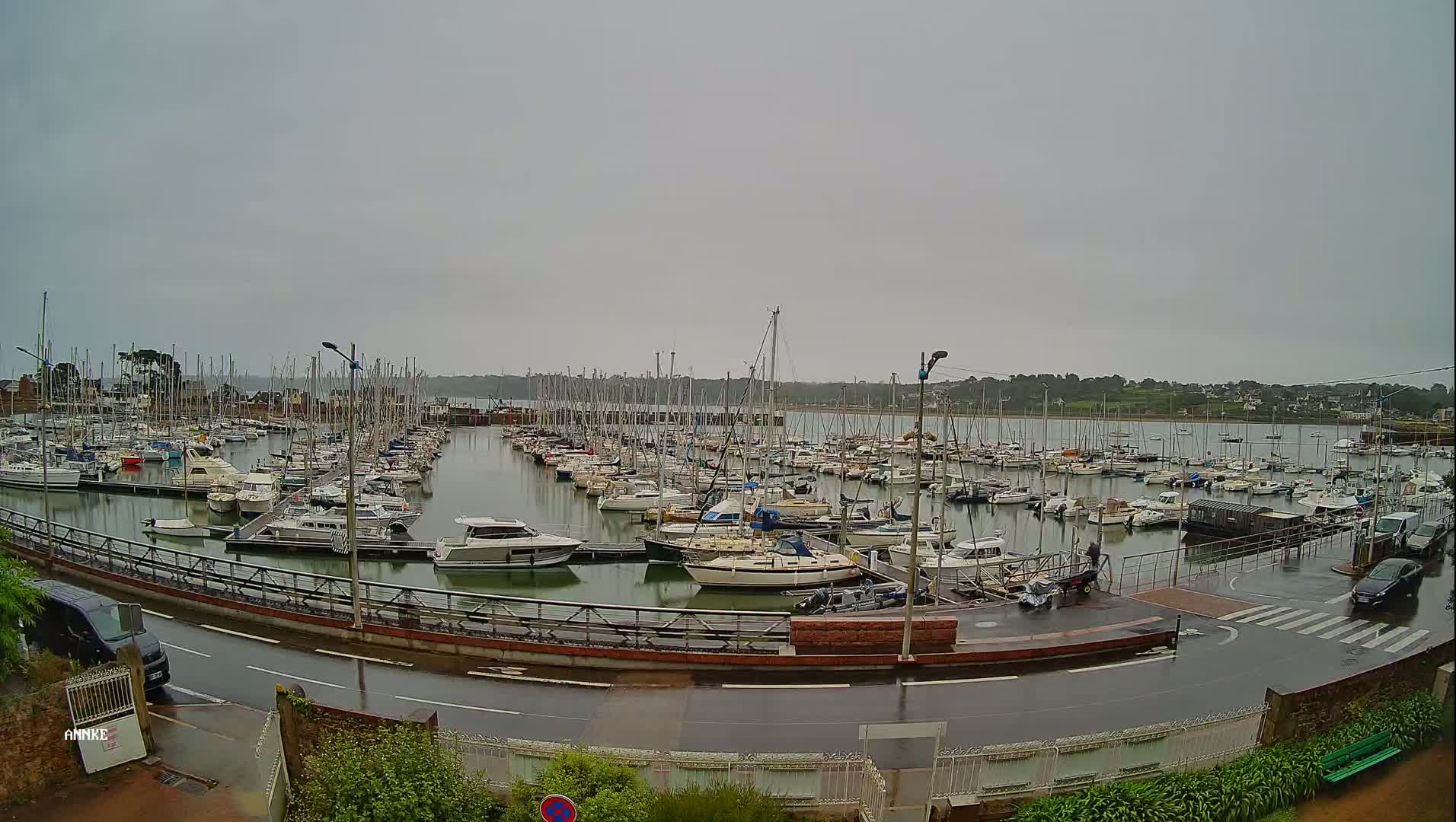 A marina filled with numerous sailboats and motorboats is seen on a rainy day.