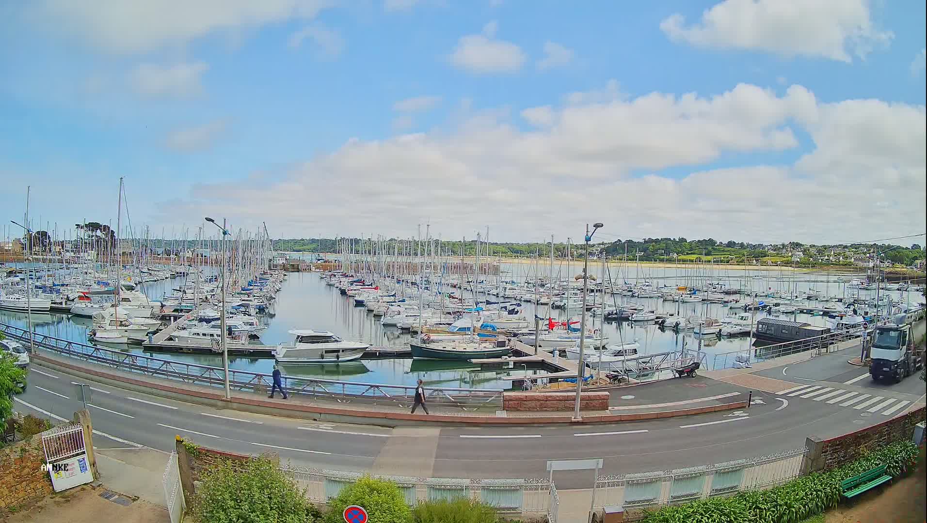 A large marina filled with numerous sailboats and motorboats is situated on calm water under a partly cloudy sky.
