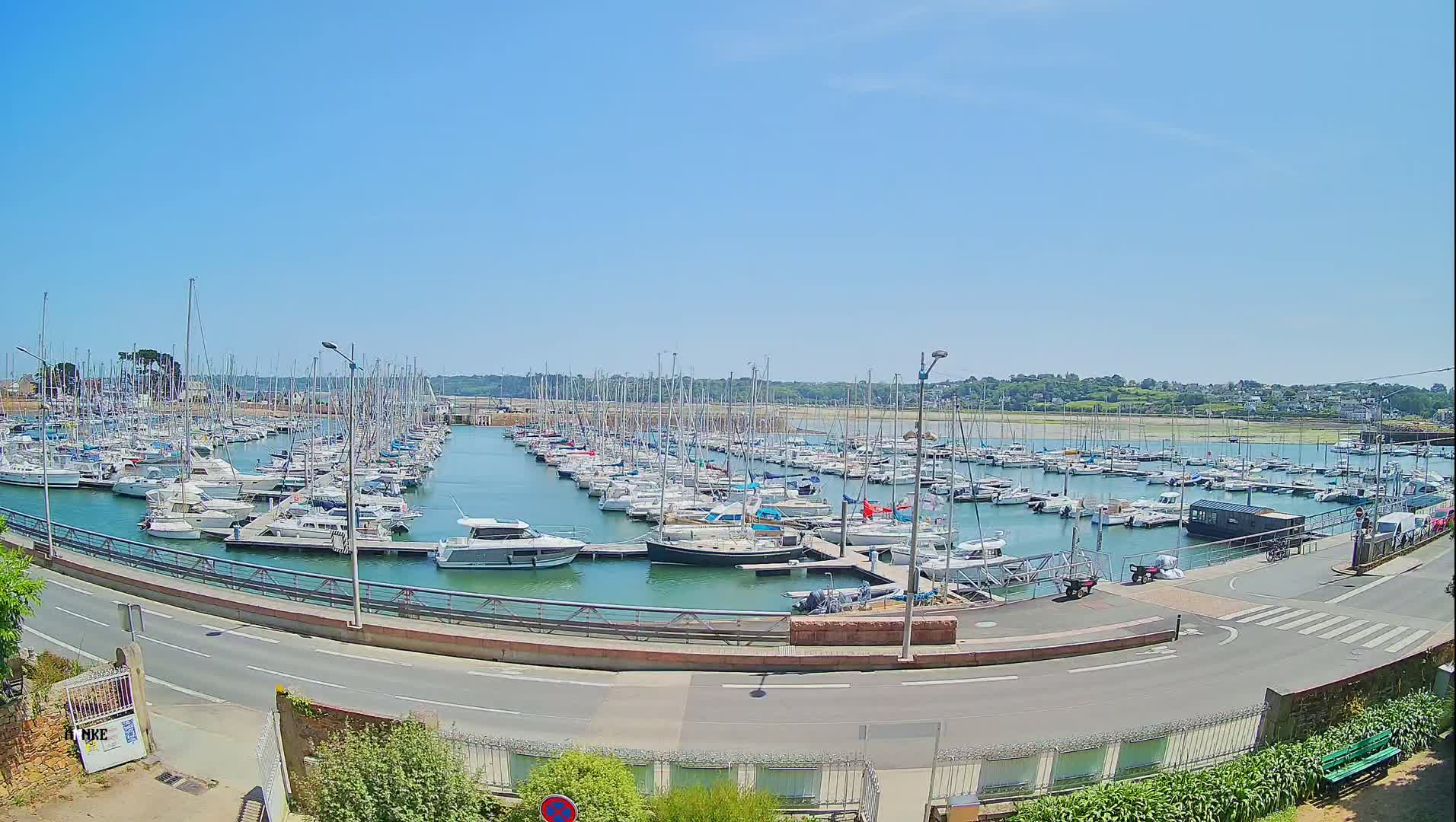 A large marina filled with numerous sailboats and motorboats is shown on a sunny day.